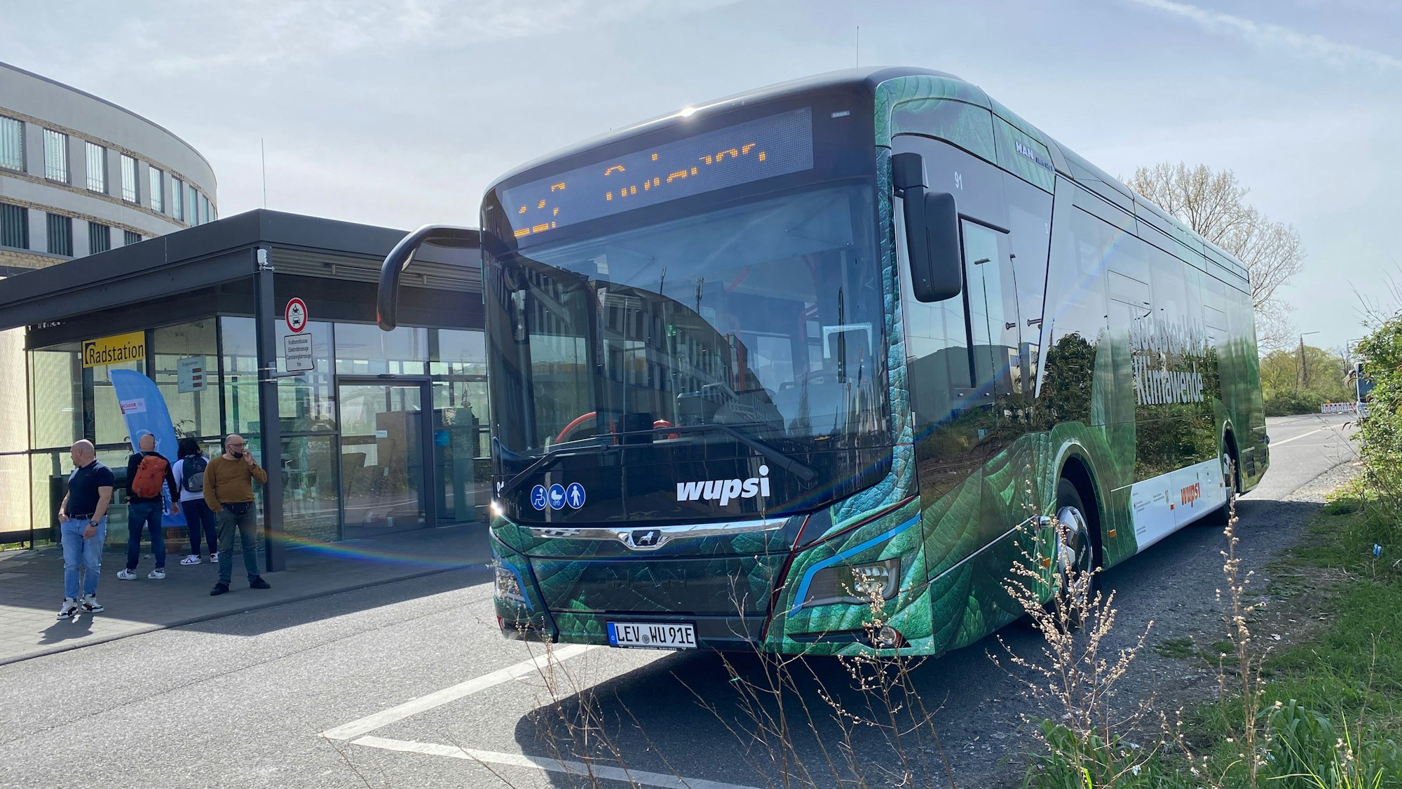 Ein grüner Wupsi-Bus steht an einer Haltestelle.
