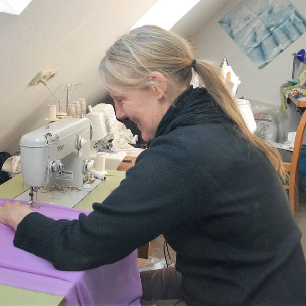 Das Foto zeigt Bekleidungsgestalterin Ursula Fischer. An ihrer Nähmaschine schneidert sie aus lila Stoff ein Kostüm.