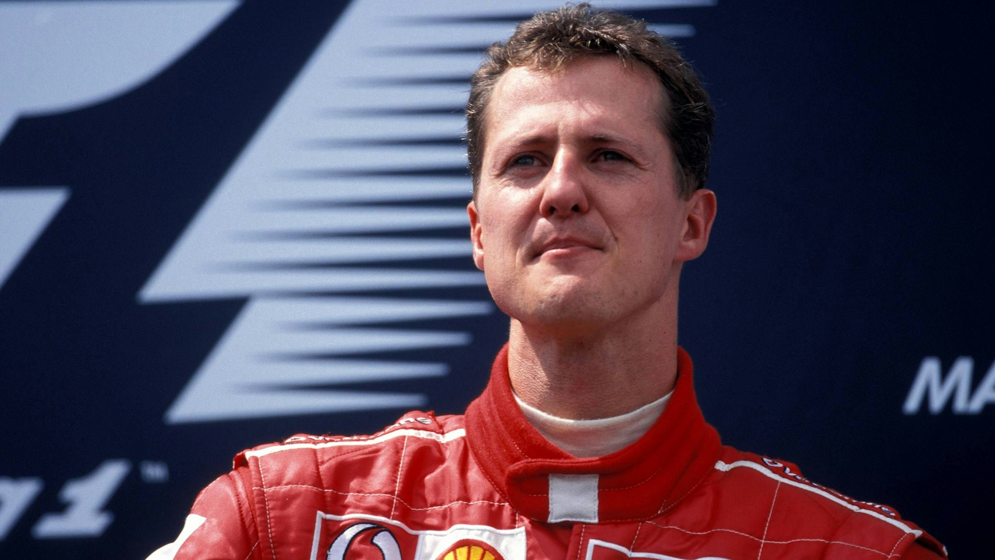 Der ehemalige Formel-1-Pilot Michael Schumacher schaut vor einem Werbebanner in die Ferne.