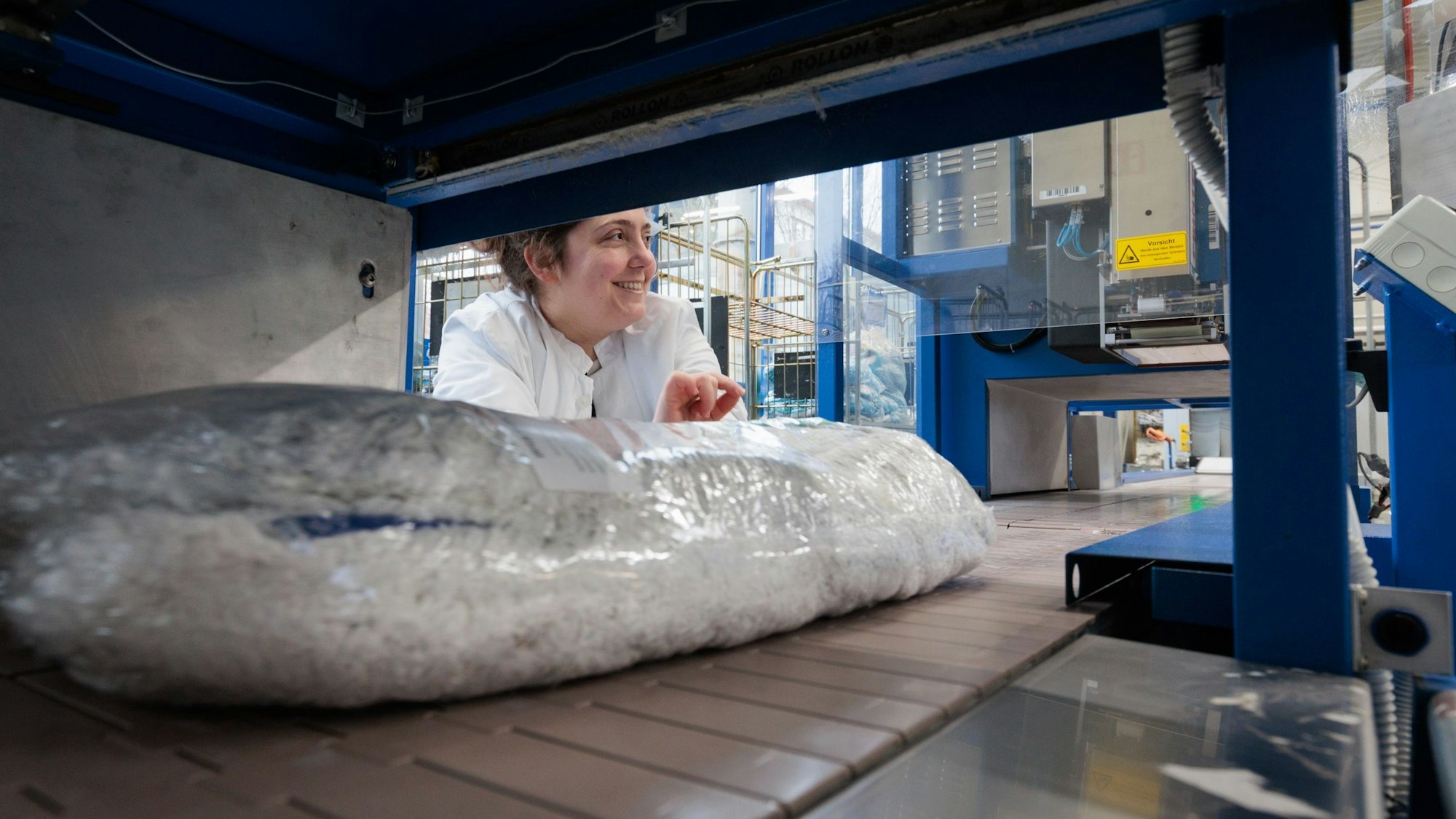 Eine Frau wird durch ein Regalfach hindurch fotografiert, sie schaut lachend zur Seite. Im Regalfach liegen verpackte Wischbezüge.