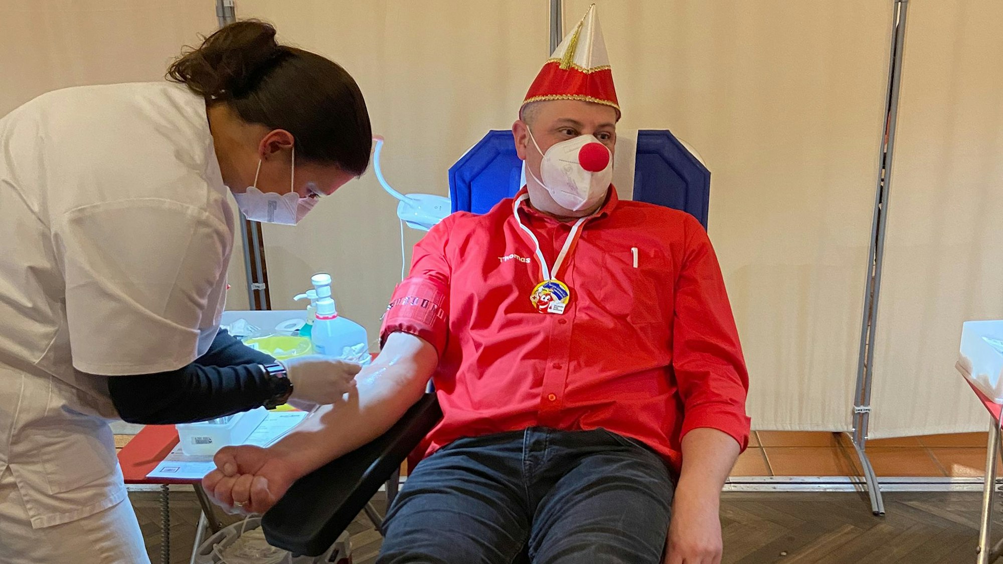 Ein Mann mit Narrenkappe lässt sich Blut abnehmen.