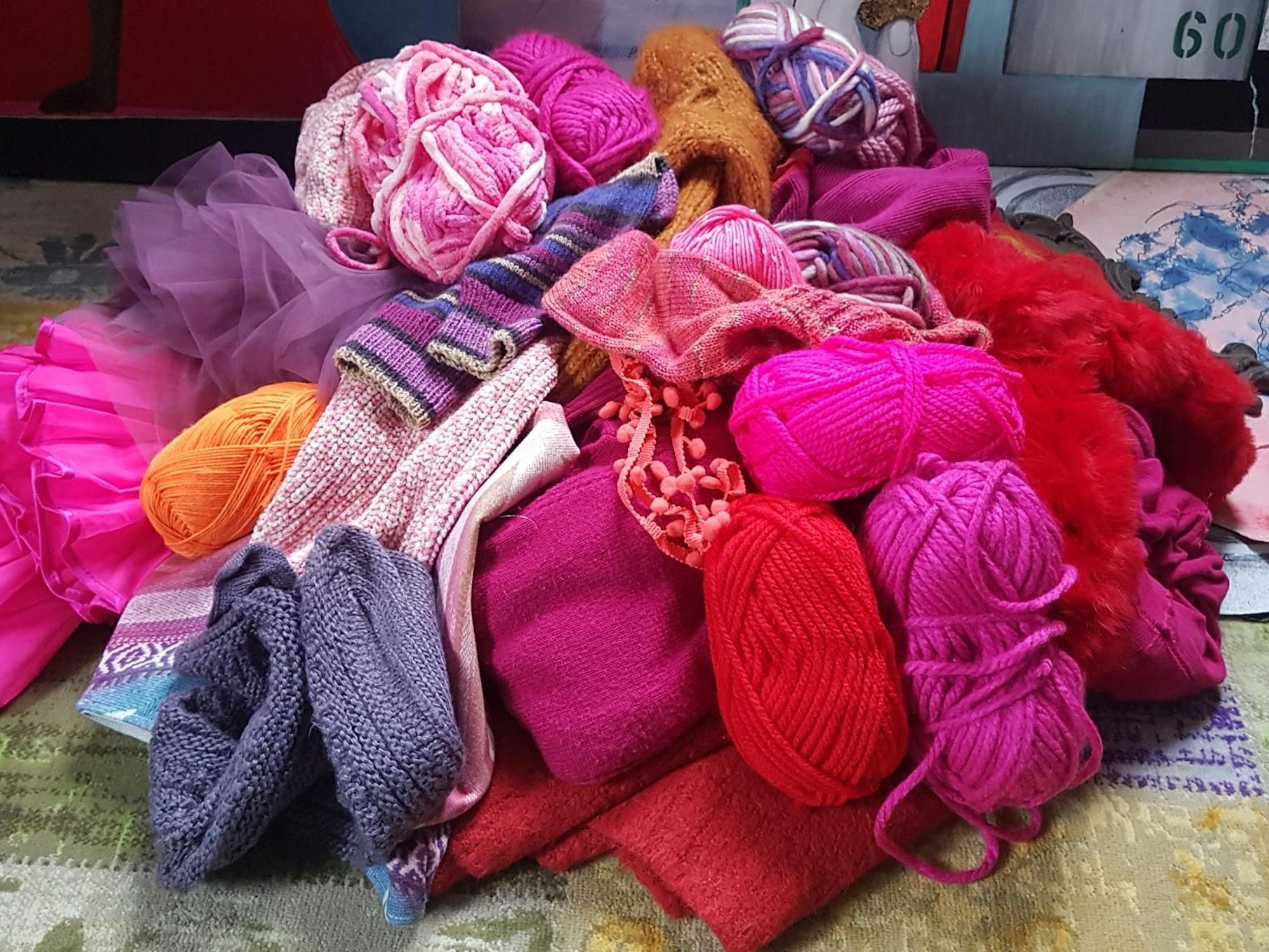 Auf einem Haufen liegen zahlreiche Wollknäule, viele von ihnen in den Farben Pink und Lila.