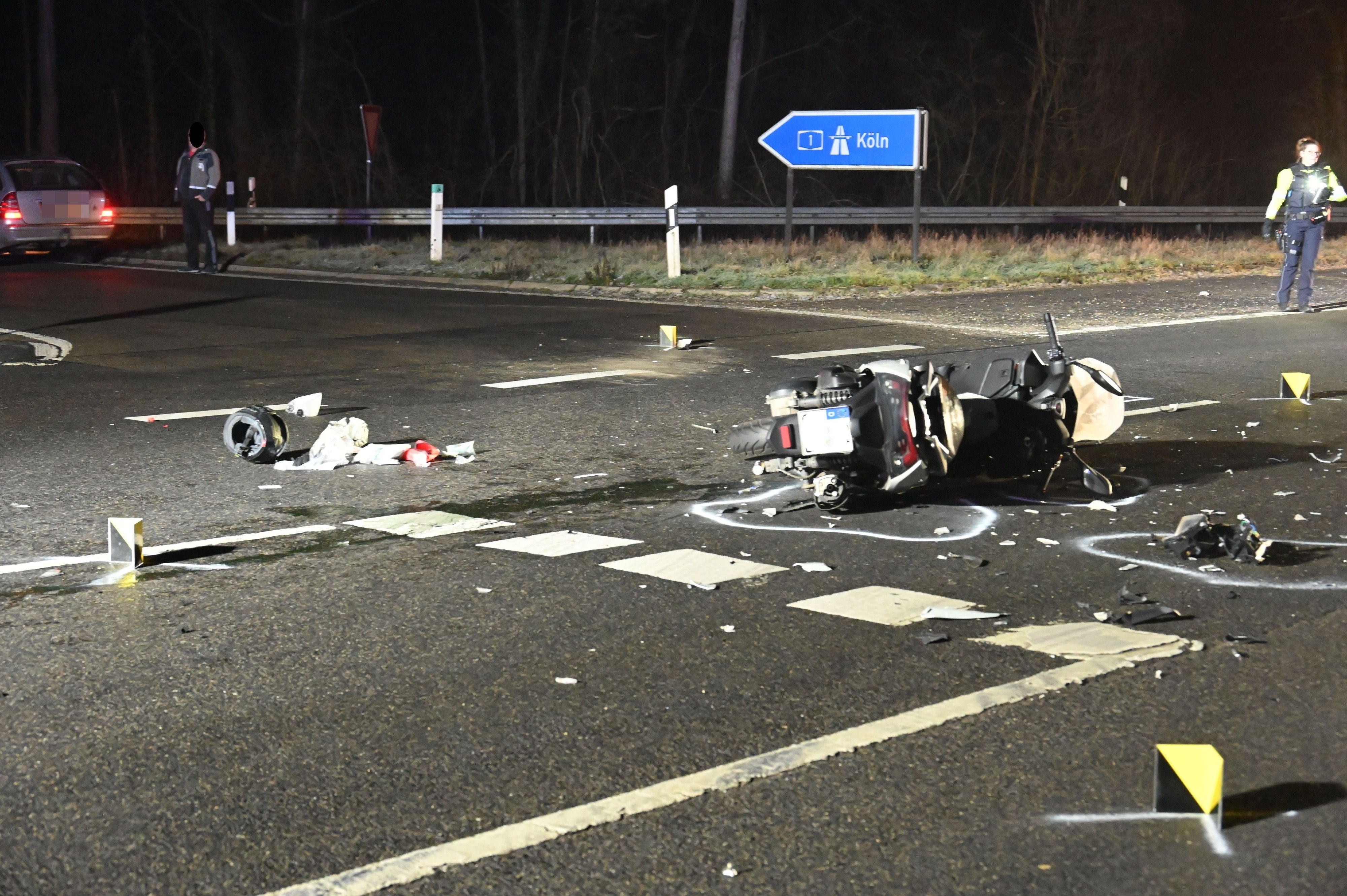 Ein schwer demolierter Roller liegt auf der Seite auf der Straße. Viele Einzelteile liegen drumherum. Sie sind mit Kreide von der Polizei markiert.