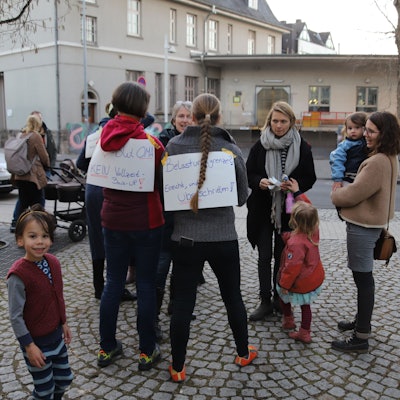 Eltern und Kinder haben sich auf einem Platz versammelt.