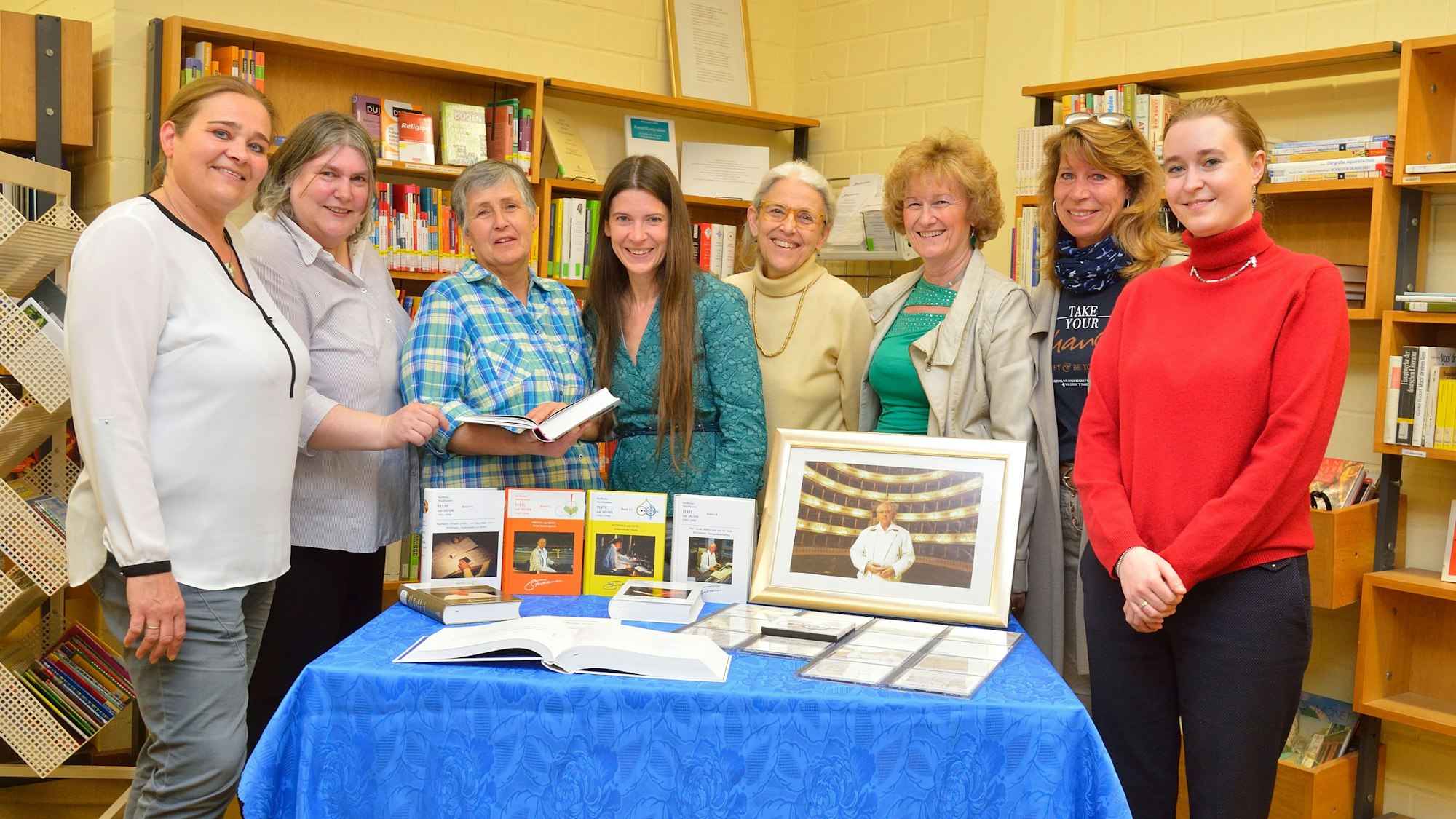 Mitarbeiterinnen und Mitarbeiter der Kürtener Bücherei stehen mit Vertretern der Stockhausen-Stiftung und der Gemeinde Kürten um einen Tisch, auf dem Bücher und Fotografien ausgelegt sind.