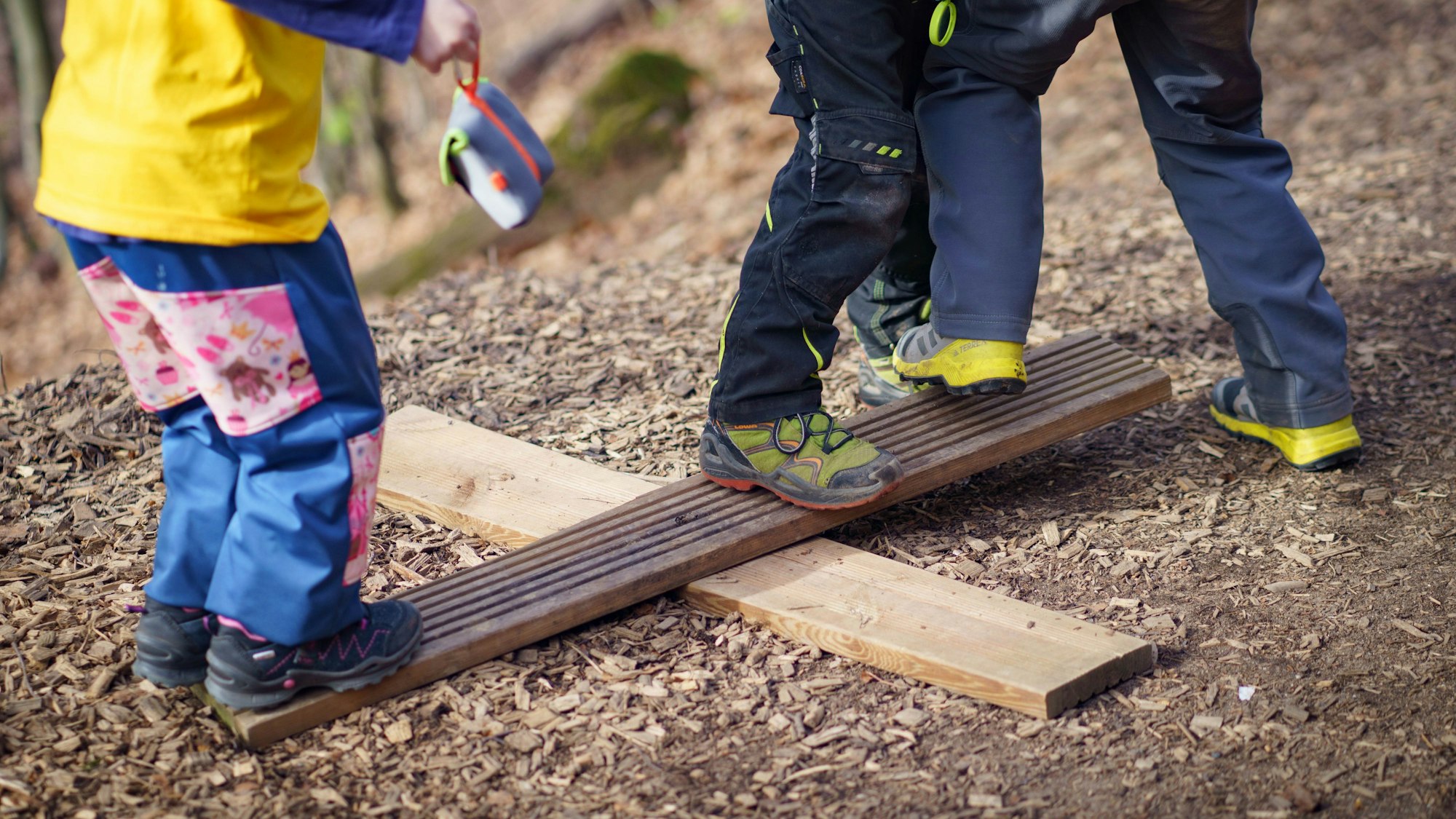 Auf einer einfachen, selbst zusammengesetzten Wippe, spielen Kinder im Waldkindergarten.