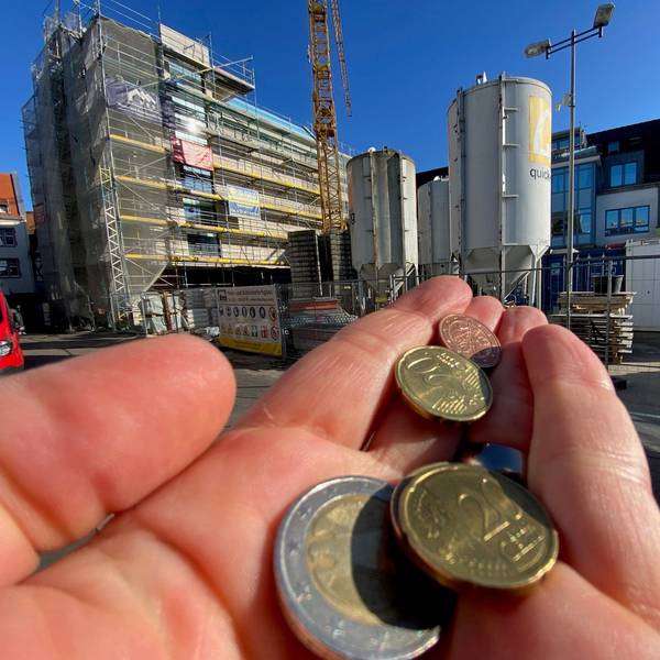Eine Hand mit Münzen. Im Hintergrund sieht man die Baustelle des Brühler Rathaus. (Symbolbild)