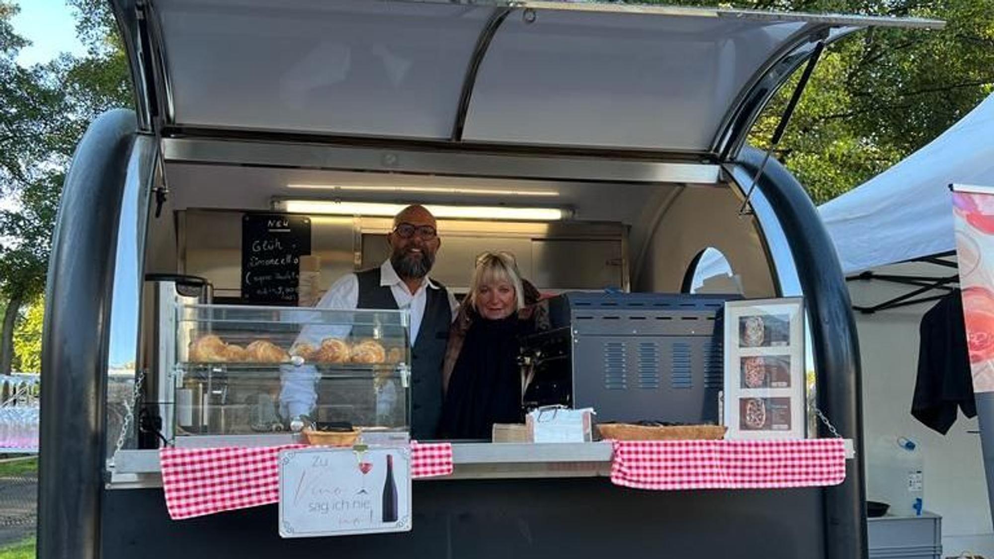 Das Ehepaar steht in seinem schwarzen Foodtruck hinter der Theke.