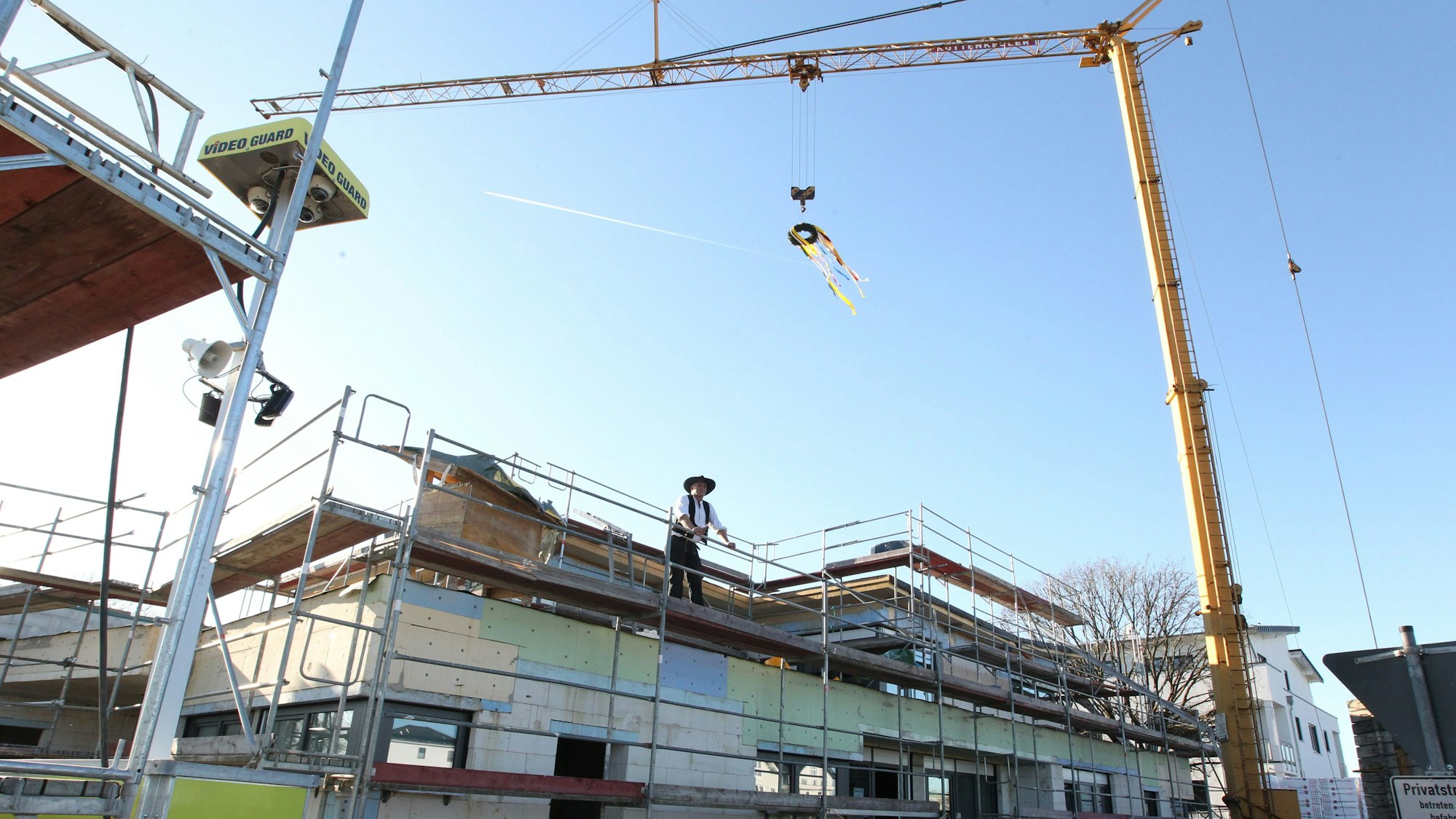 Baustelle eines Gebäude-Neubau mit Gerüsten und einem Baukran. Ein Mann lehnt sich an eine Gerüst-Reling.