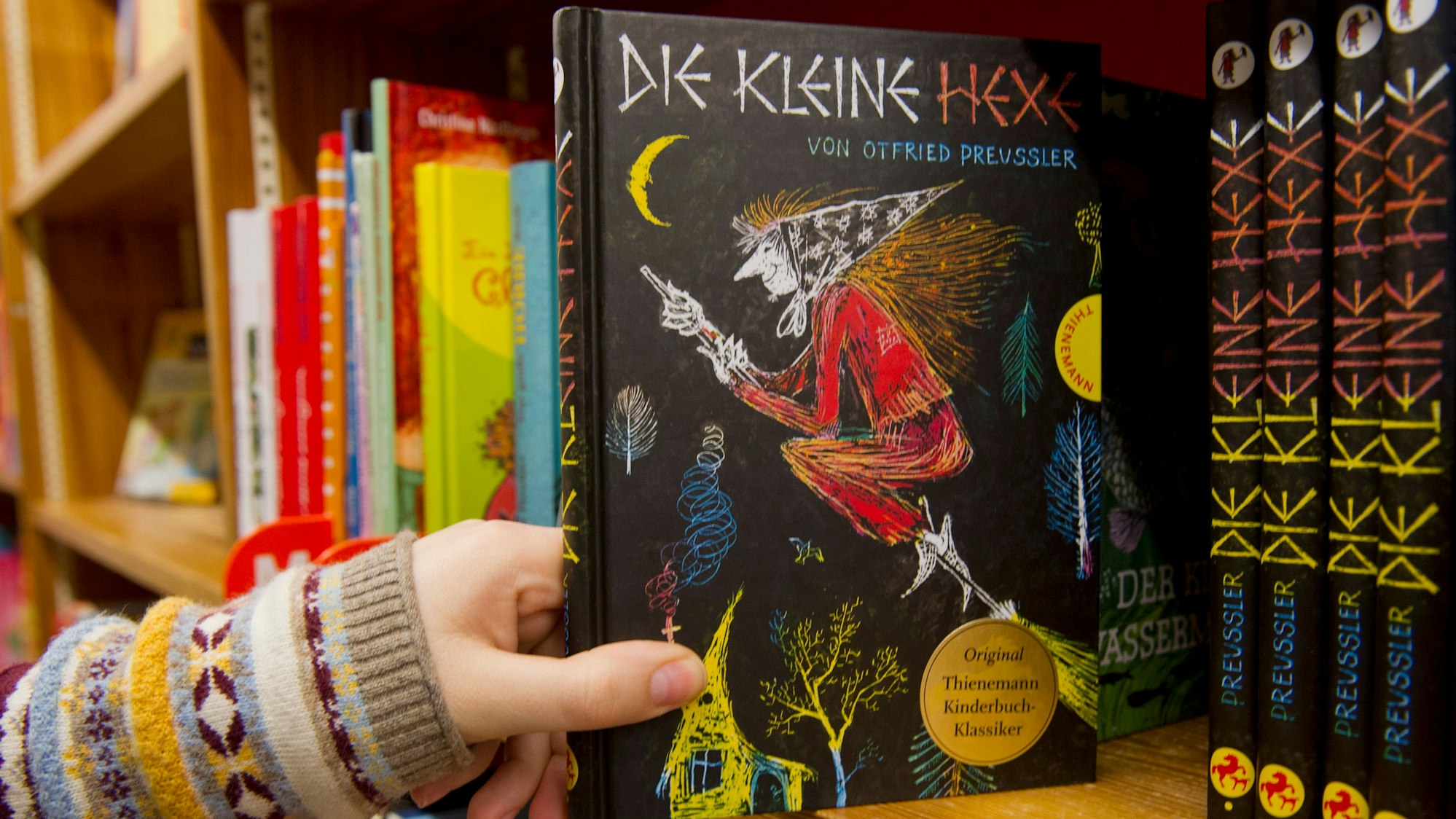 Das Kinderbuch "Die kleine Hexe" von Otfried Preußler wird aus dem Regal gezogen.