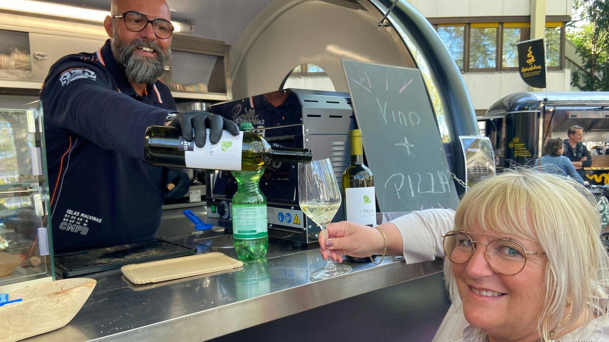 Umberto schenkt seiner Frau ein Glas Wein am Foodtruck ein.