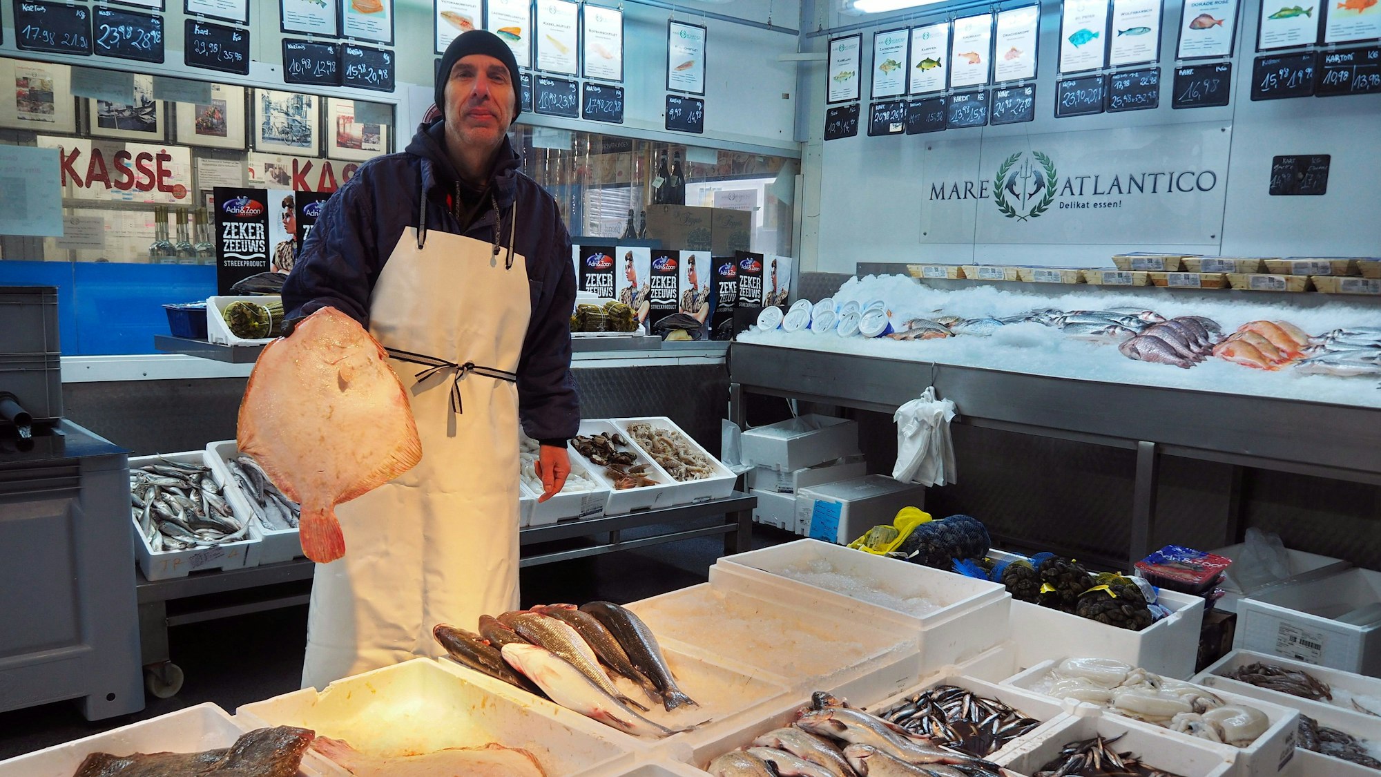 Der Verkäufer von Mare Atlantico hat einen Fisch in der Hand und steht in seiner Verkaufshalle.