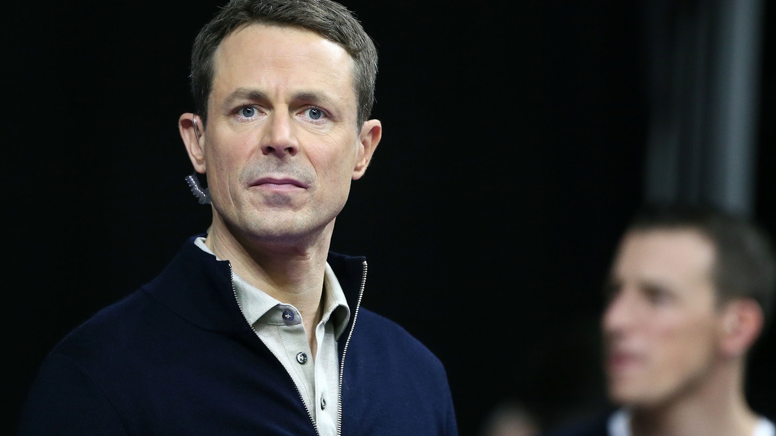 Moderator Alexander Bommes steht mit einem Mikrofon in Hemd und Pullover bei einer Live-Übertragung der ARD vor der Kamera.