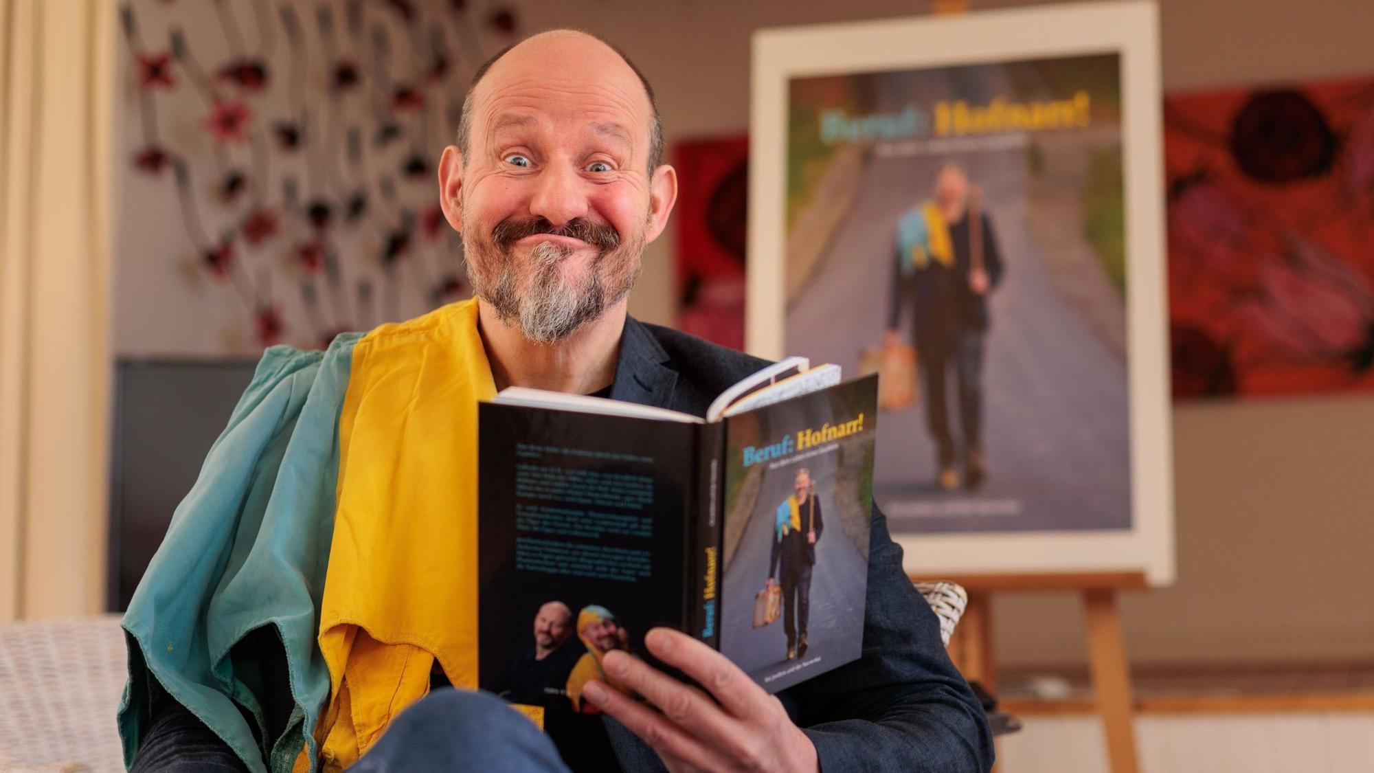 Kai Jordens schneidet eine Grimasse, während er sein Buch hält.