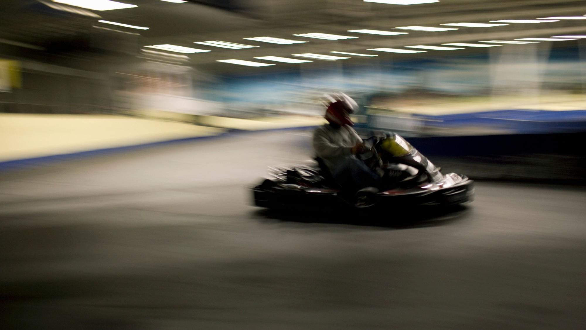 Eine Person mit einem Helm sitzt in einem Kart. Das Bild ist leicht verschwommen.