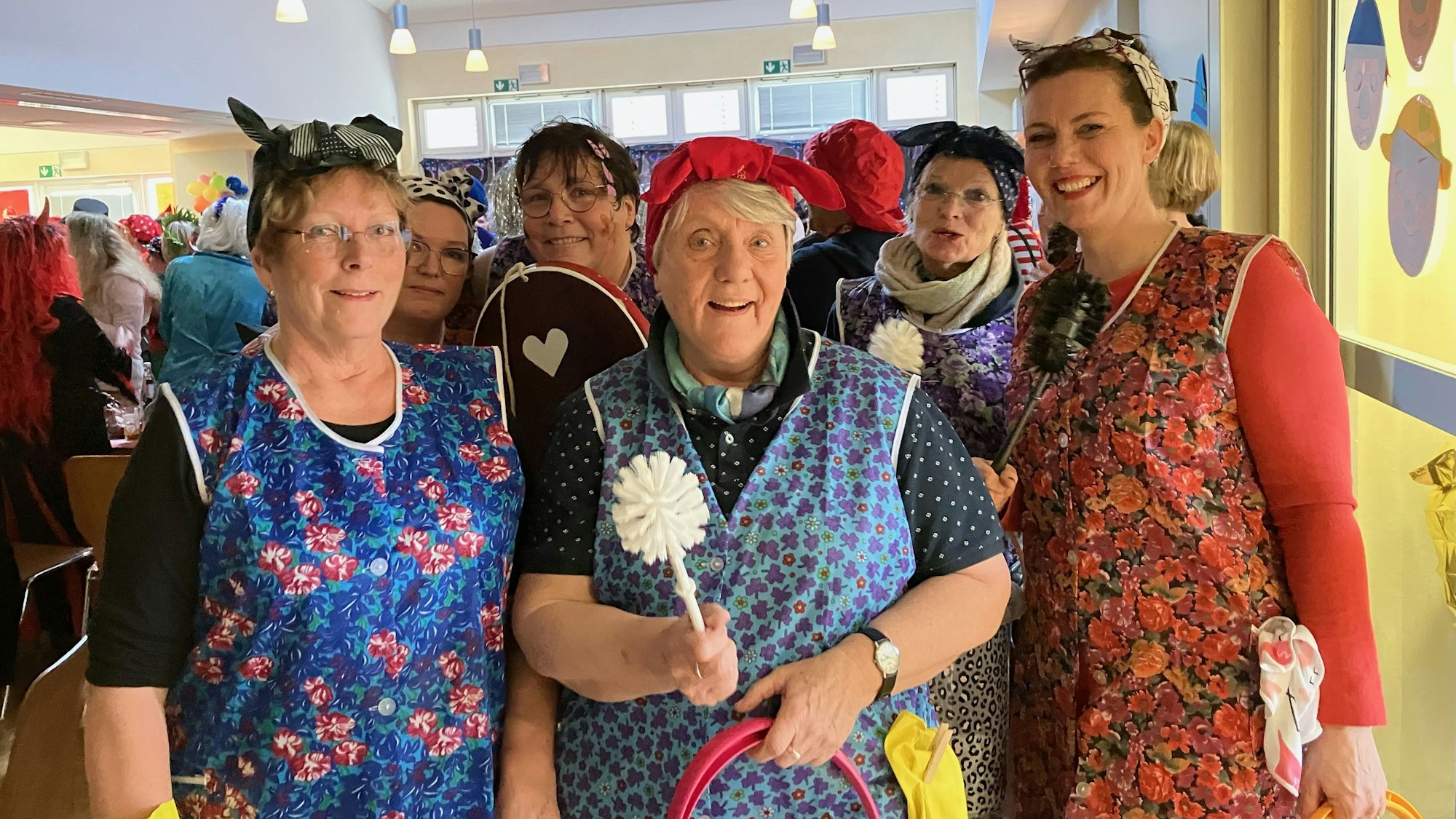 Mehrere Frauen stehen zusammen. Sie alle haben sich als Reinigungskräfte verkleidet, mit Kittel, Haarband sowie Klobürsten und Putzeimern in der Hand.