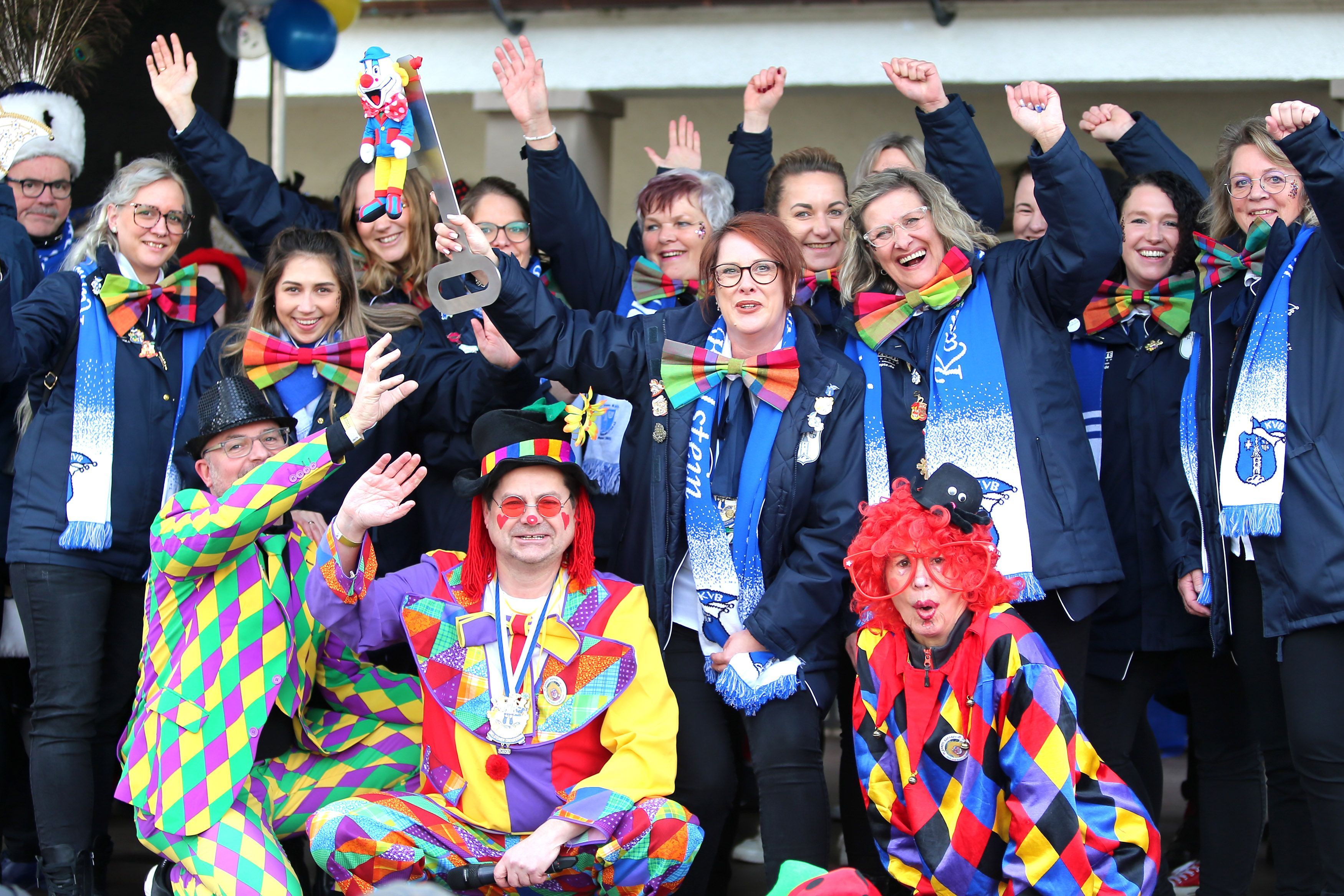 Ein als bunter Clown verkleideter Bürgermeister sitzt inmitten Feiernder und ebenfalls verkleideter Frauen.