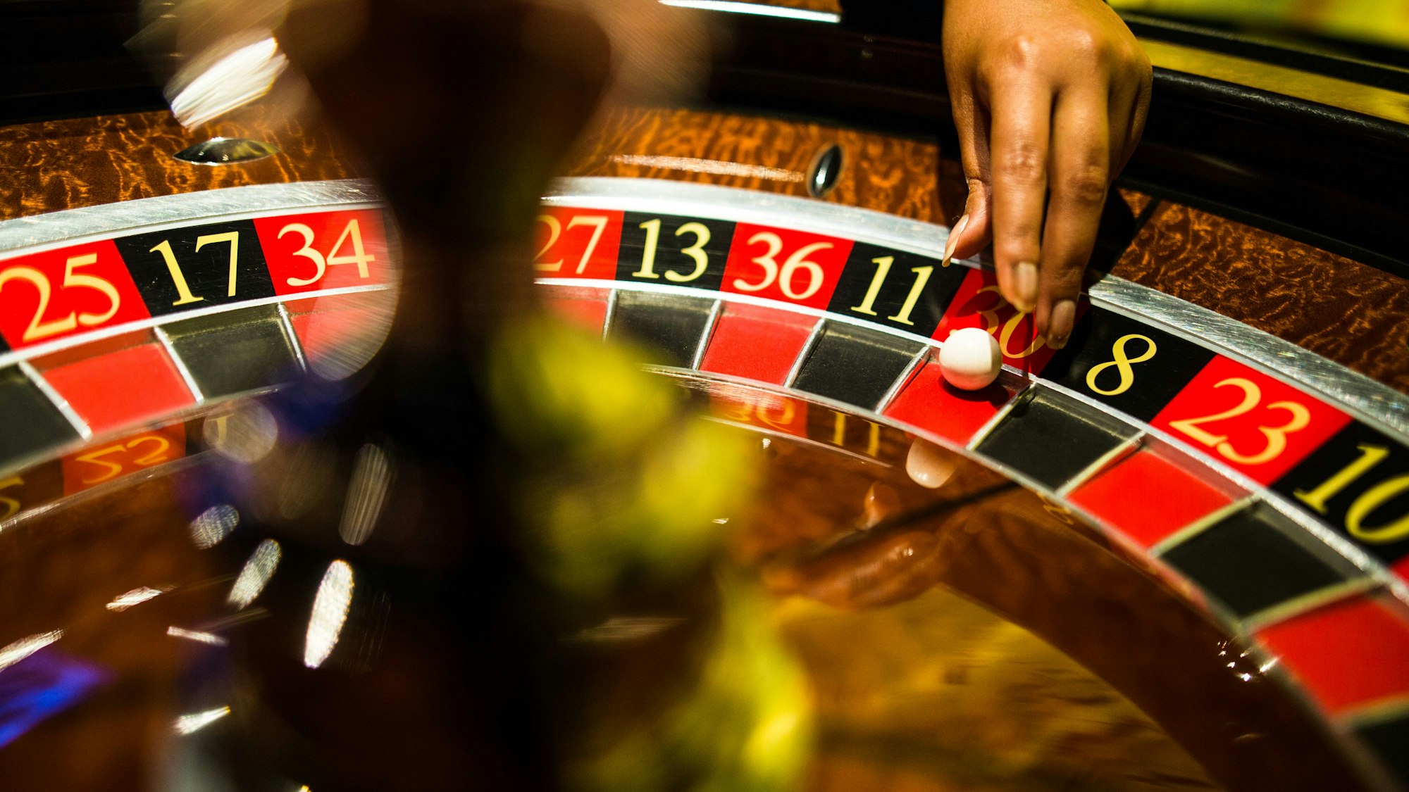 Eine Person greift mit der Hand beim Spiel Roulette nach einer Kugel, die auf Rot liegt.