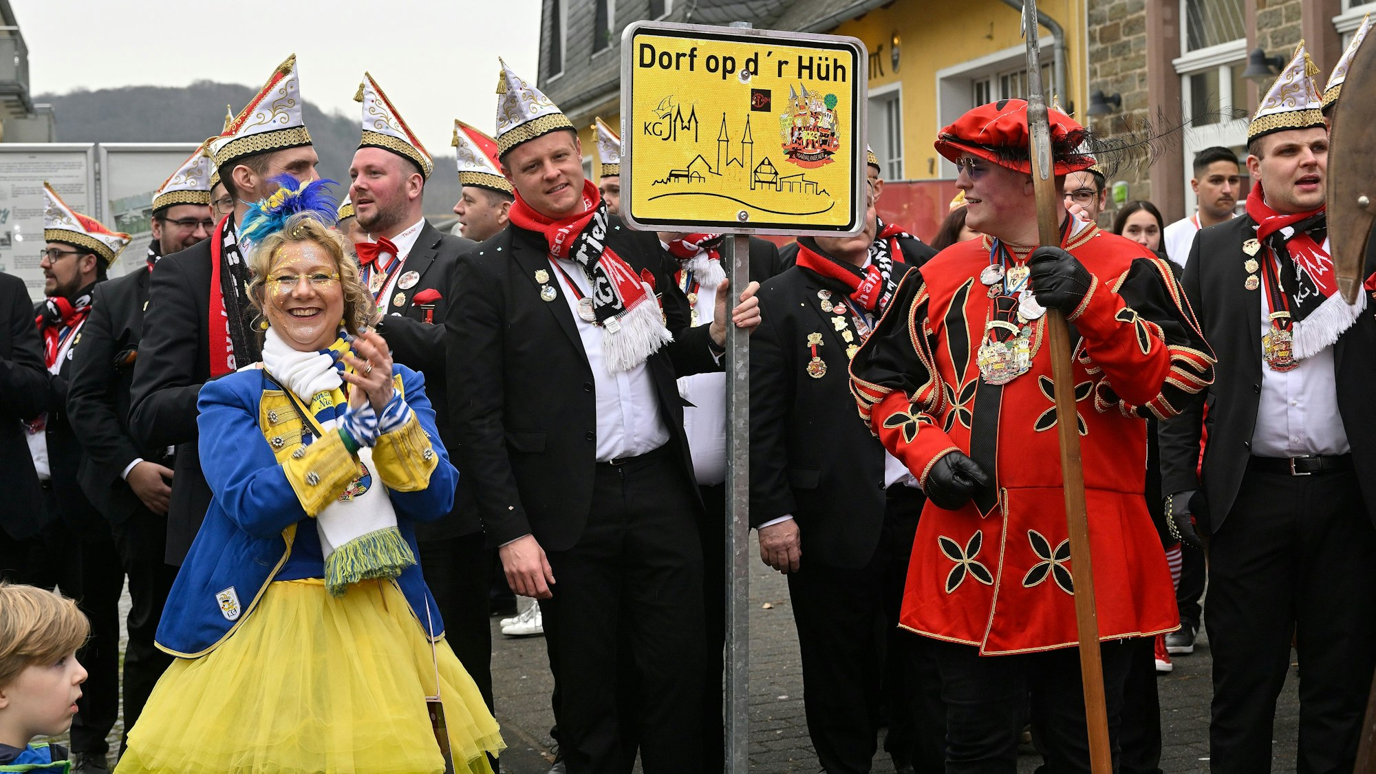 Narren stehen mit einem Straßenschild auf dem Platz.