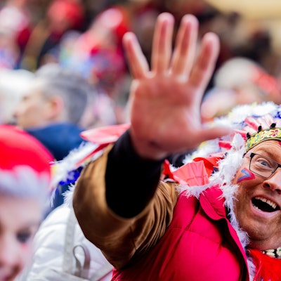 Karnevalisten feiern an Weiberfastnacht die Eröffnung des Straßenkarnevals auf dem Alter Markt. Ein Karnevalist trägt eine bunte Perücke und hält eine Kamera in die Hand.