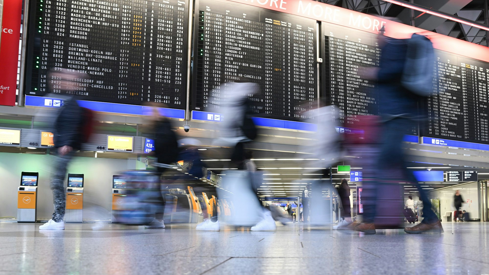 Fluggäste gehen mit ihrem Koffern im Terminal 1 des Frankfurter Flughafens an der Anzeigetafel mit den Abflügen vorbei (Aufnahme mit längerer Verschlusszeit).