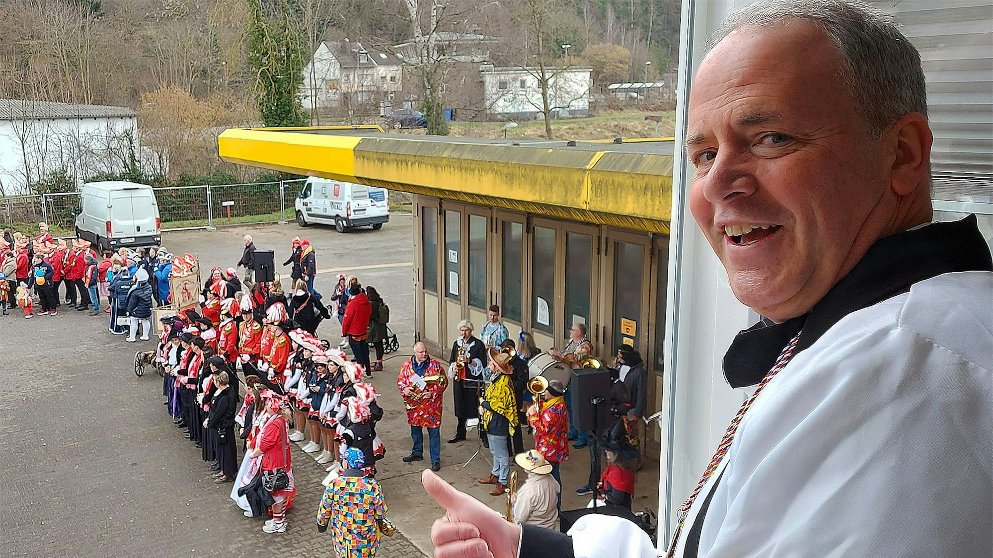 Bürgermeister Hermann-Josef Esser betrachtet aus einem Fenster in der ersten Etage die Jecken auf dem Platz.