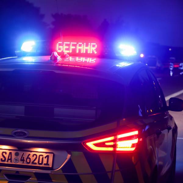 Ein Polizeiauto hat das Blaulicht an, außerdem ist in roten Buchstaben „Gefahr“ auf dem Dach des Einsatzwagens zu lesen. Im Hintergrund ist eine Unfallstelle zu sehen. (Symbolbild)