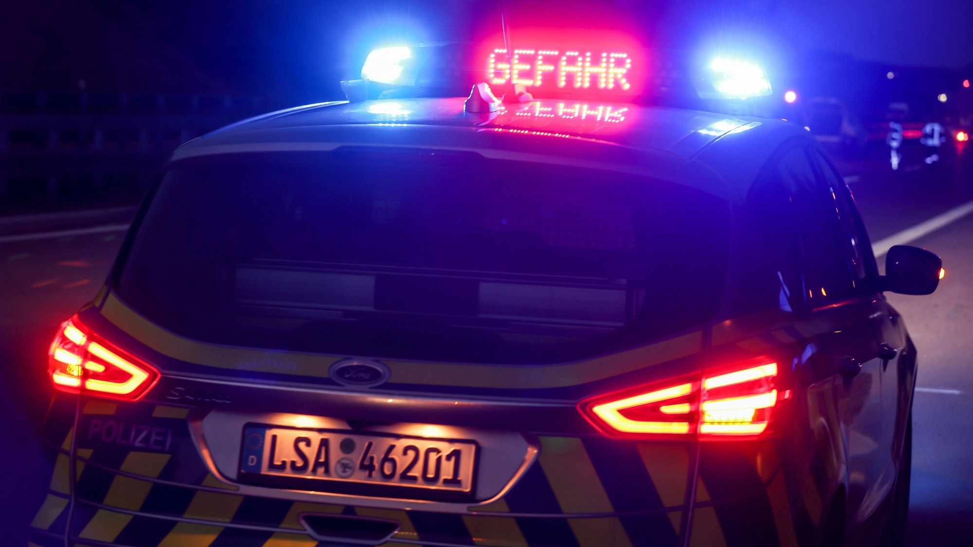 Mit Blaulicht und der Anzeige „Gefahr“ steht ein Polizeifahrzeug nach einem schweren Verkehrsunfall auf der Autobahn 14 bei Halle-Trotha.(Symboldbild)