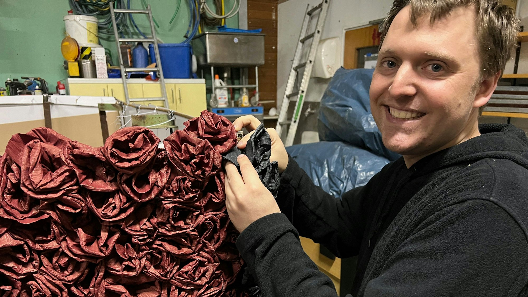 Marc Horst befestigt Papierröschen am Prunkwagen.