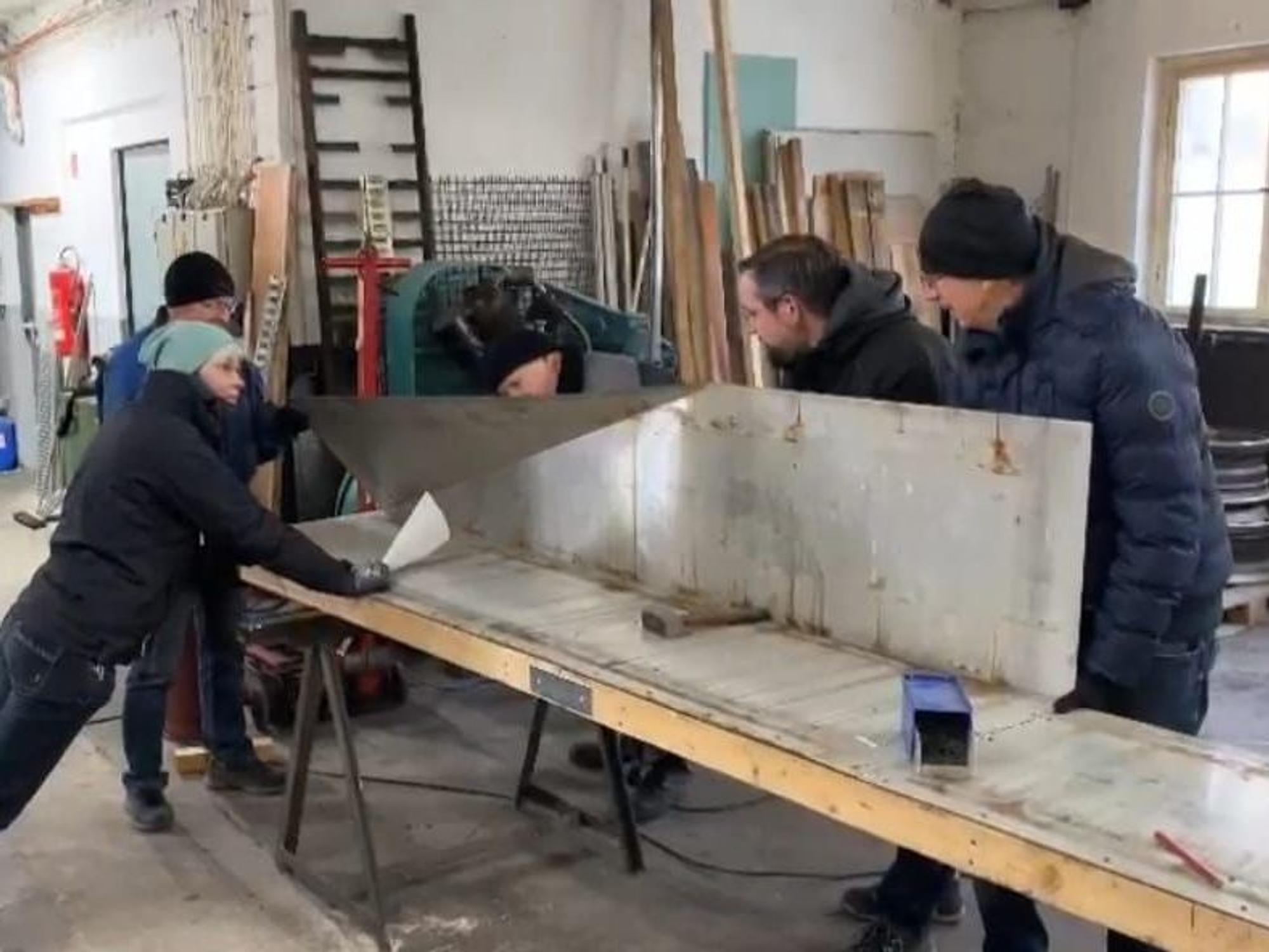 Blick in einen Werkstatt, in der fünf Menschen an einem Bob bauen.