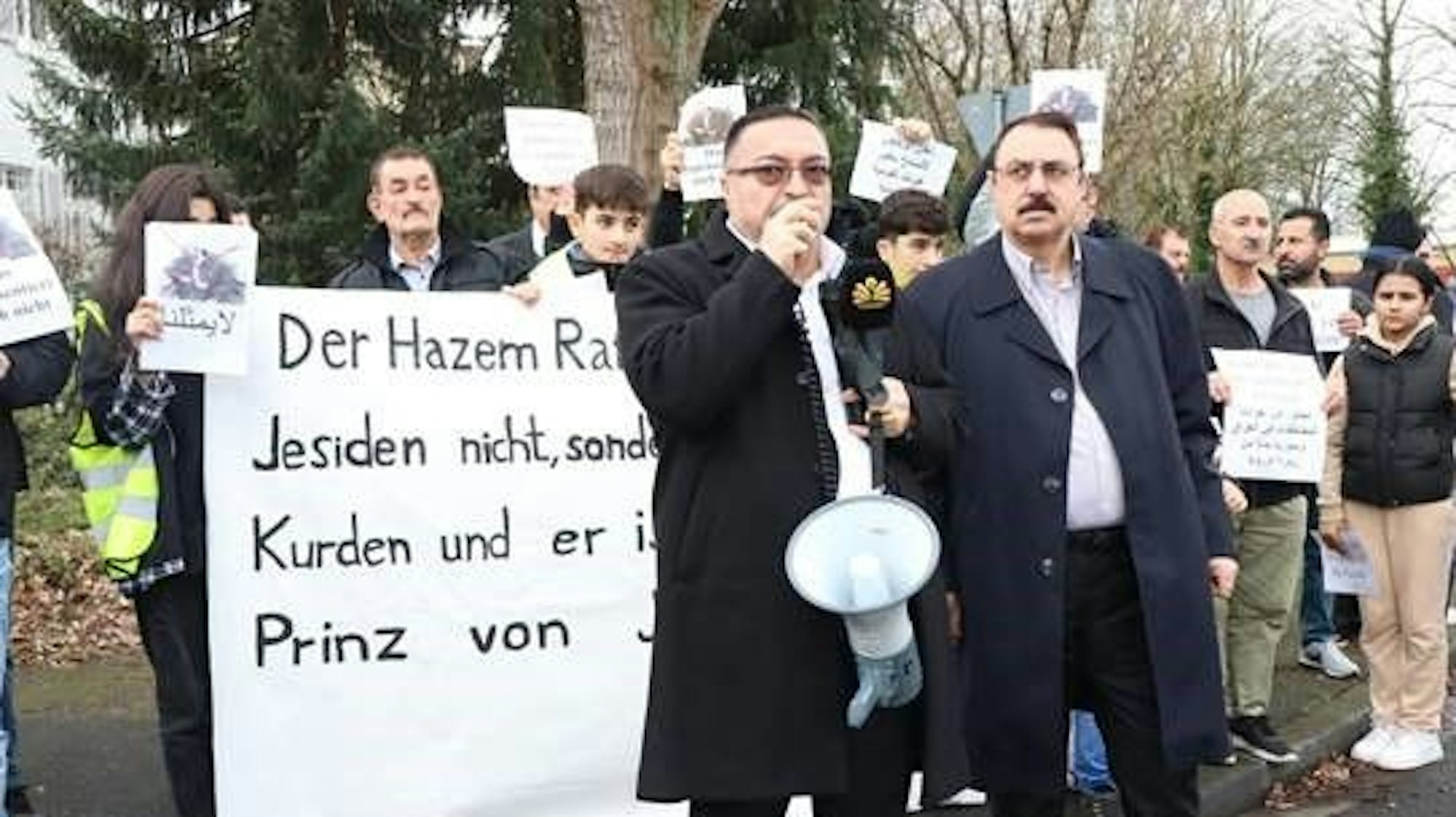 Mehrere Demonstrierende stehen hinter dem Redner und halten Schilder.