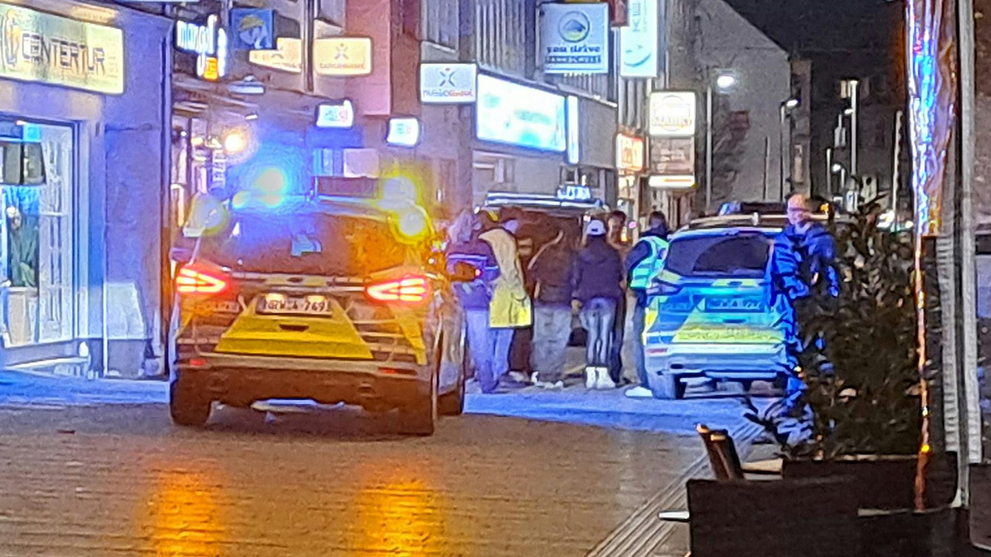 Zwei Streifenwagen stehen mit Blaulicht in der Bergisch Gladbacher Fußgängerzone. Polizeibeamte stehen bei einer Ansammlung von Menschen.