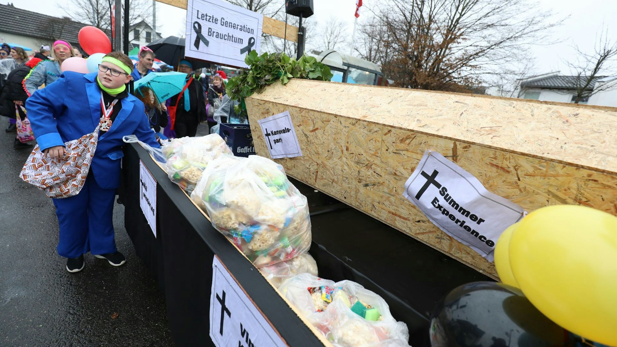 „Letzte Generation Brauchtum“ steht auf einem Schild am Wagen des Buben- und Mädelsvereins, Die jungen Leute haben einen großen Sarg auf dem Wagen installiert und tragen so symbolisch das Brauchtum zu Grabe.