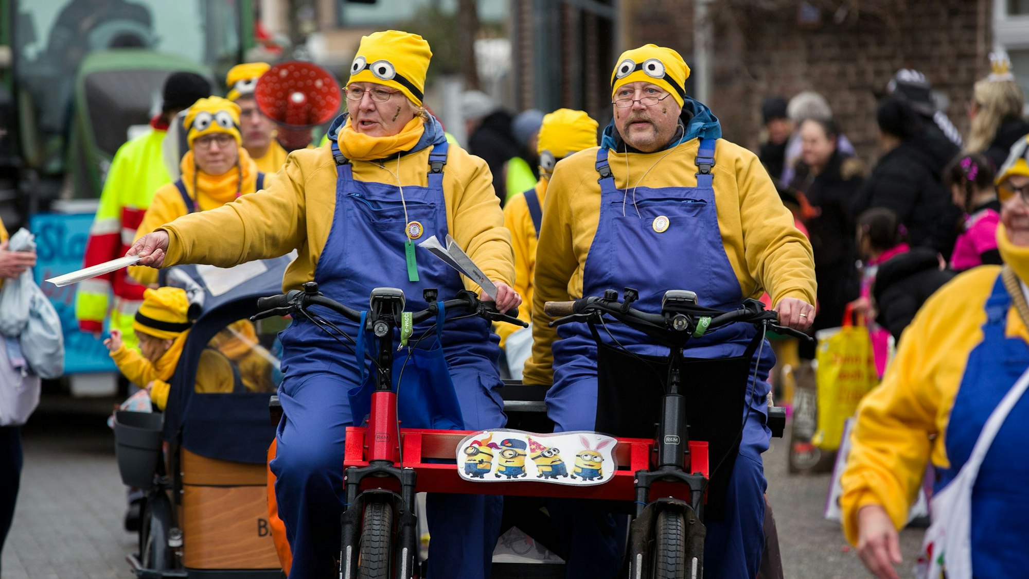 Menschen in Minions-Anzügen fahren auf einem Fahrrad über eine Straße.