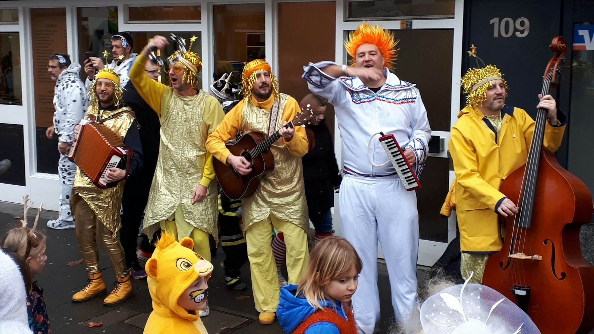 Ein Band steht mit verschiedenen Instrumenten vor einem Gebäude, die Musiker sind verkleidet.