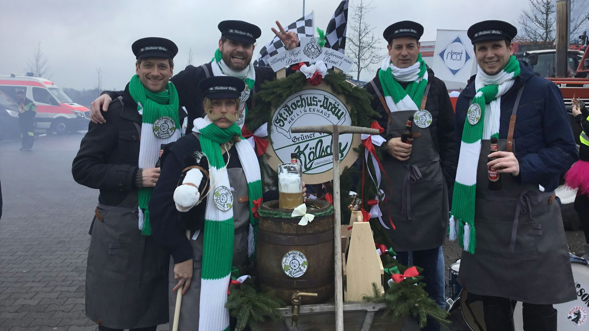 Fünf Männer mit blau-grünen Schals stehen um ein Bierfass, das auf einem Wagen montiert ist.