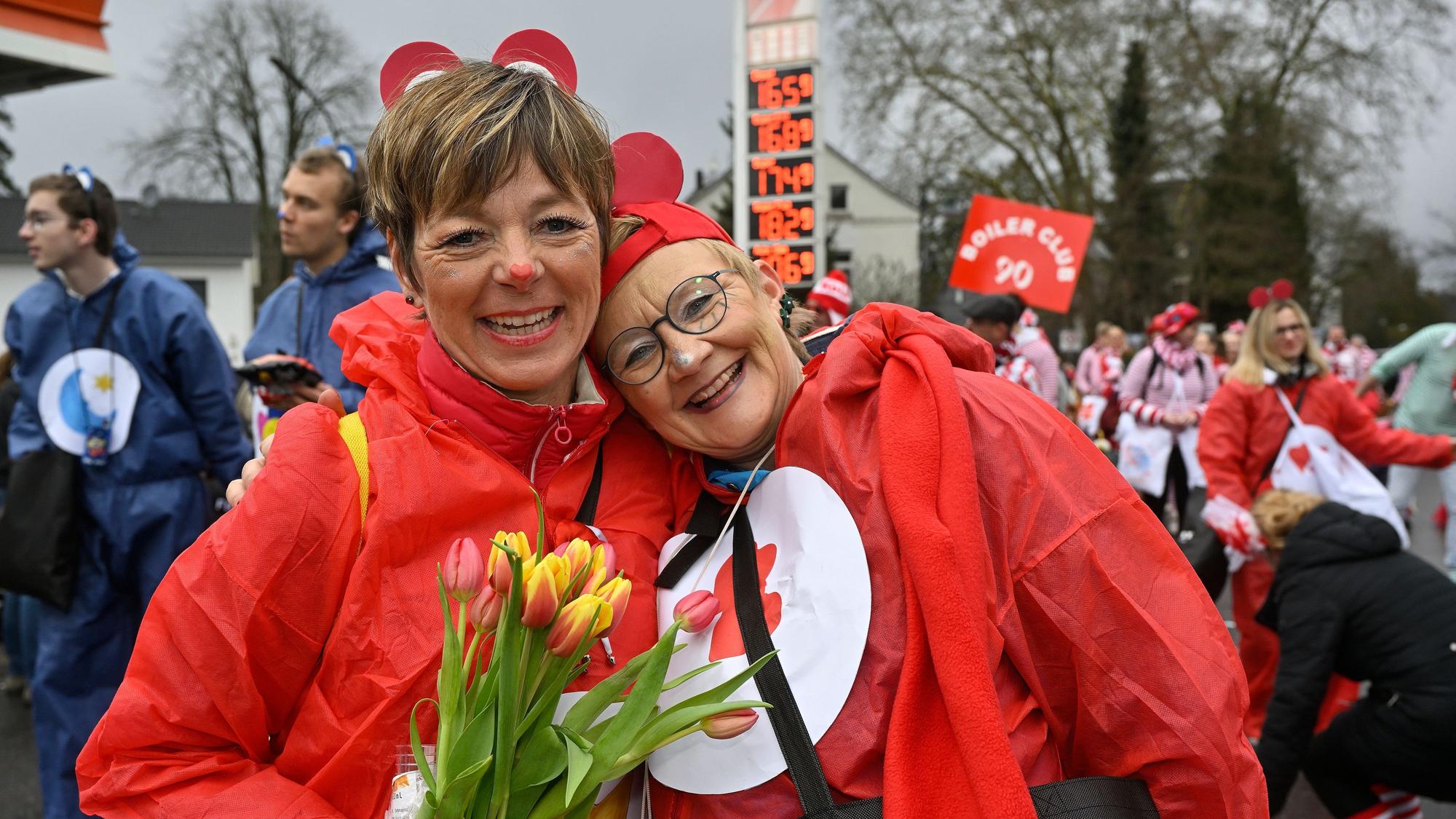 Zwei rot verkleidete Frauen lächeln Arm in Arm in die Kamera.