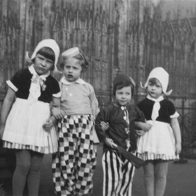 Ein Schwarzweißbild zeigt vier Kinder, die Arm in Arm in einer Reihe stehen.