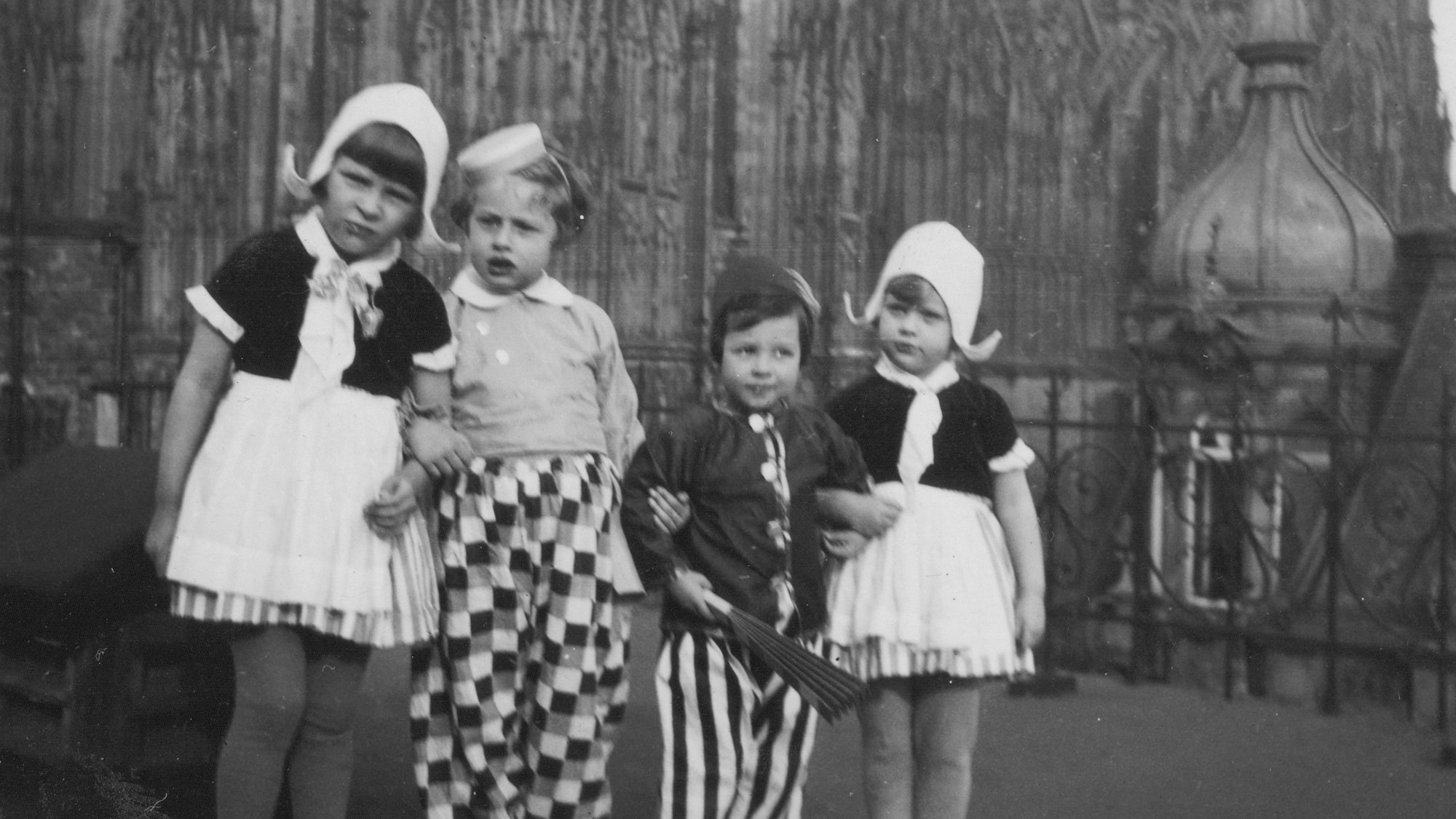 Ein Schwarzweißbild zeigt vier Kinder, die Arm in Arm in einer Reihe stehen.