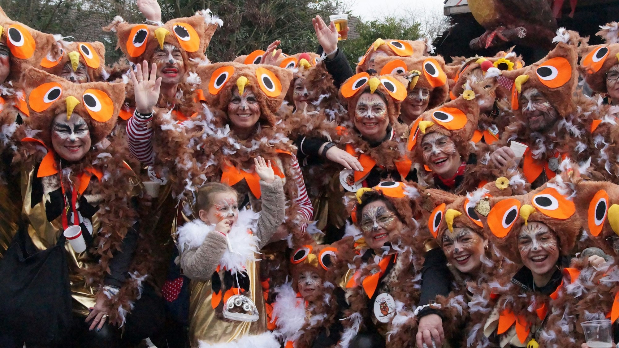 Eine Gruppe von Menschen in einem Eulenkostüm mit Federn an der Kleidung und selbstgemachten Eulenhüten auf dem Kopf posieren für ein Gruppenbild.