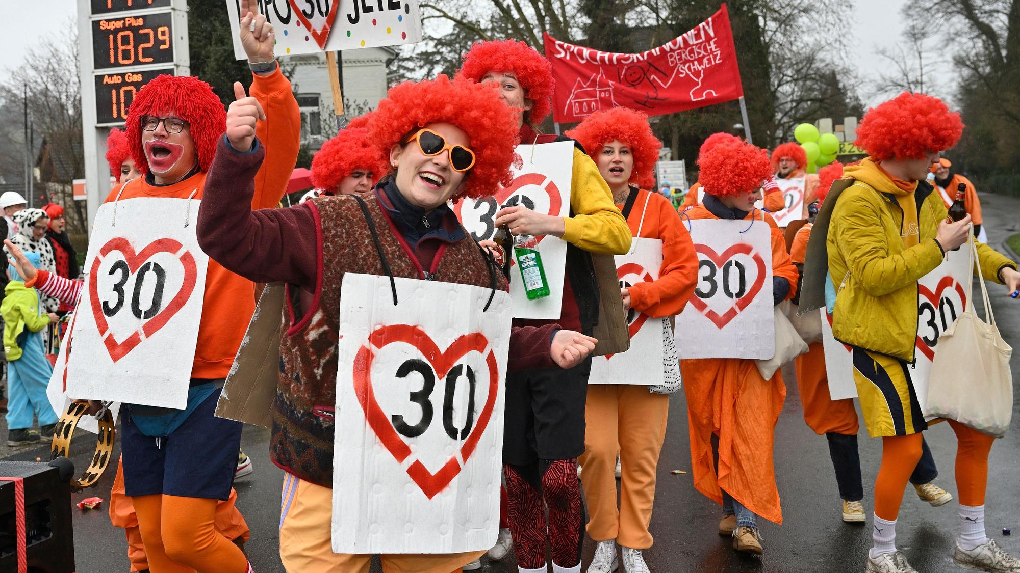 Jecke tragen rote Perücken und Schilder mit der Zahl 30 sowie roten Herzen darum drauf.