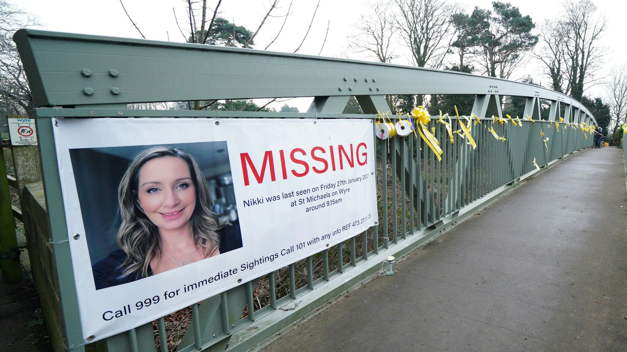 Ein Plakat mit einem Vermisstenaufruf für Nicola Bulley und gelbe Bänder mit Hoffnungsbotschaften, die an einer Brücke über den Fluss Wyre befestigt sind.