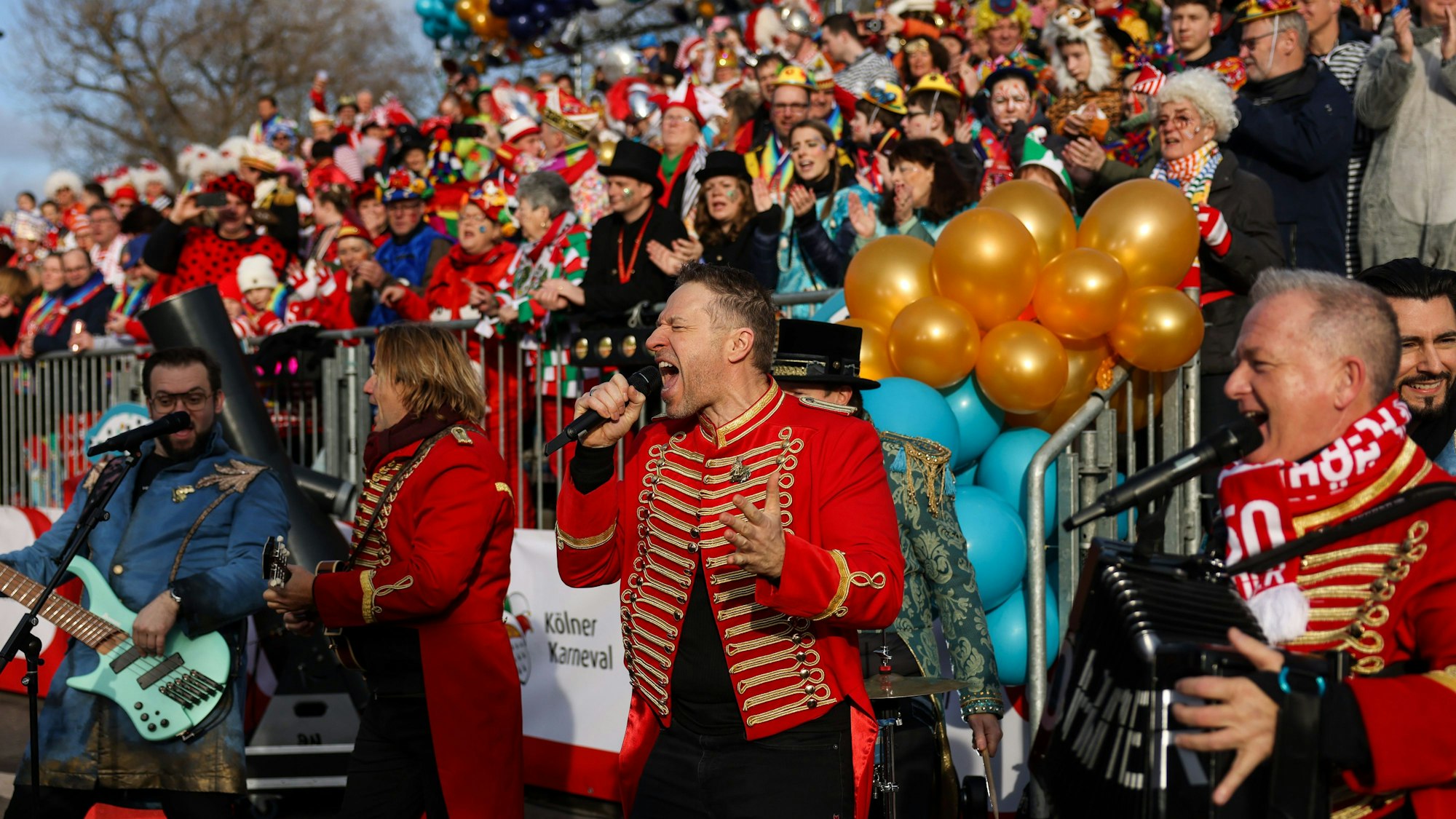 Die Höhner treten vor einer Tribüne gefüllt mit Karnevalisten auf.