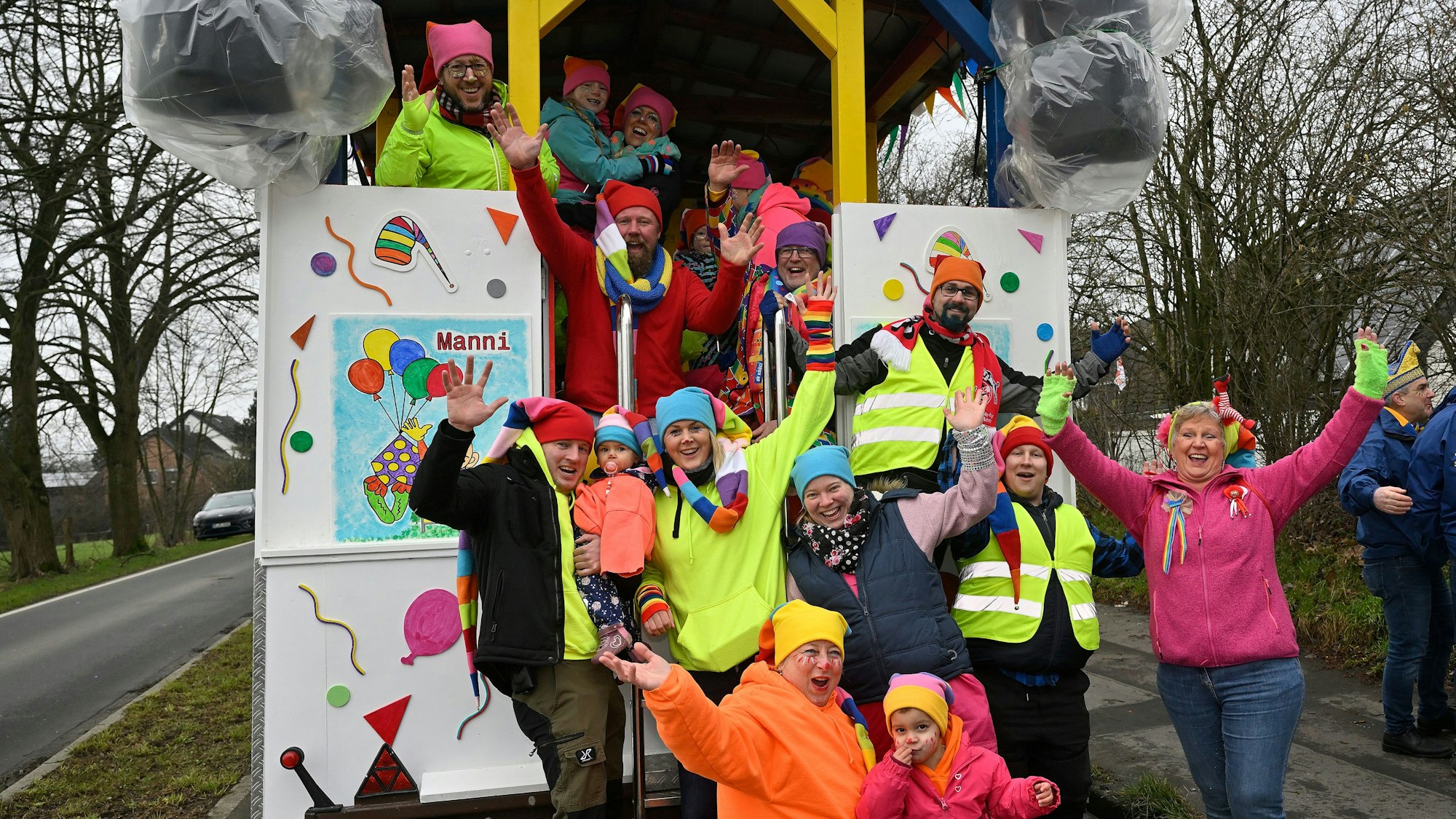 Eine Gruppe mit bunten Mützen steht an ihrem Festwagen und jubelt.