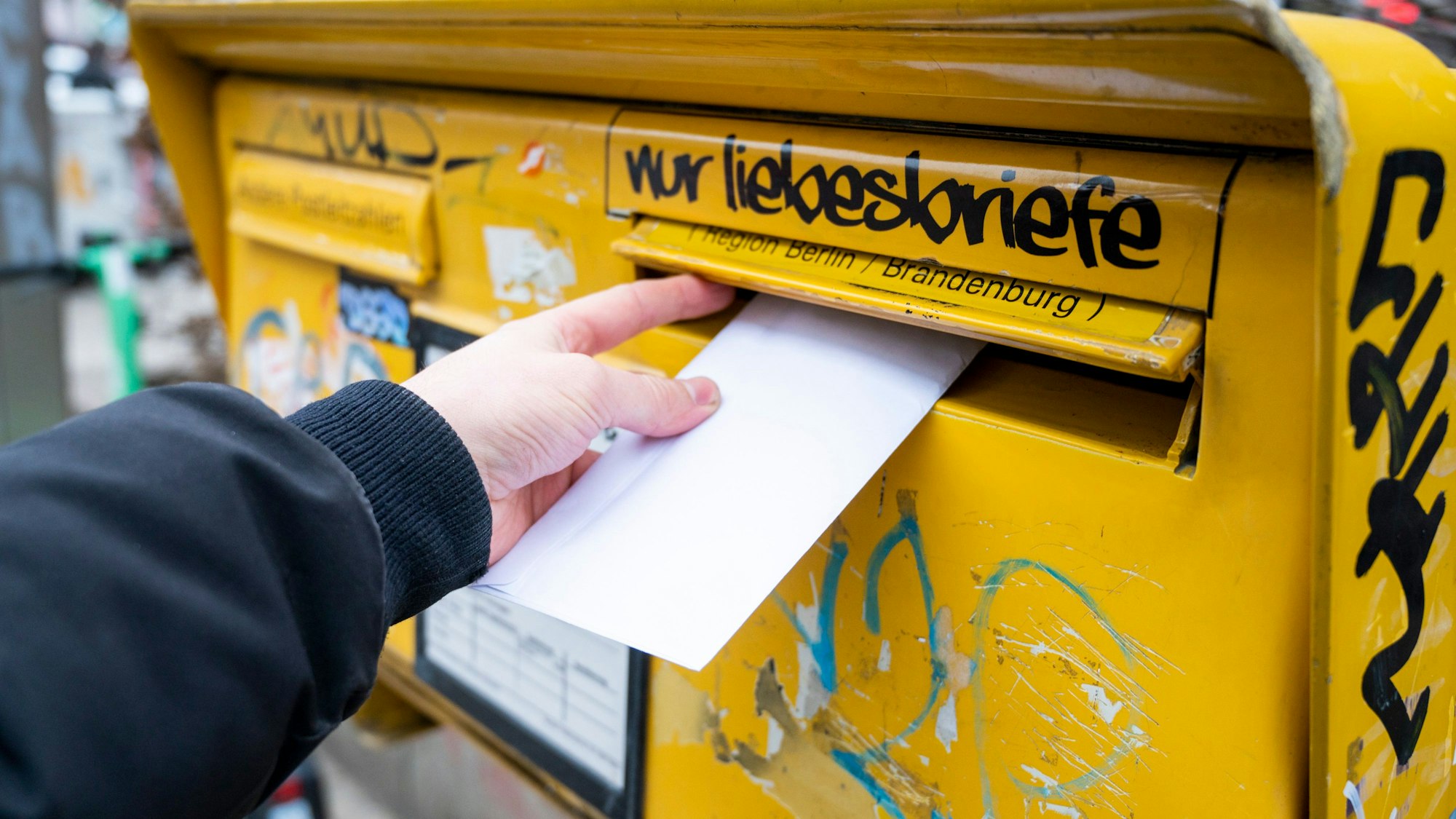 Ein Mann wirft einen Brief in einen Briefkasten.