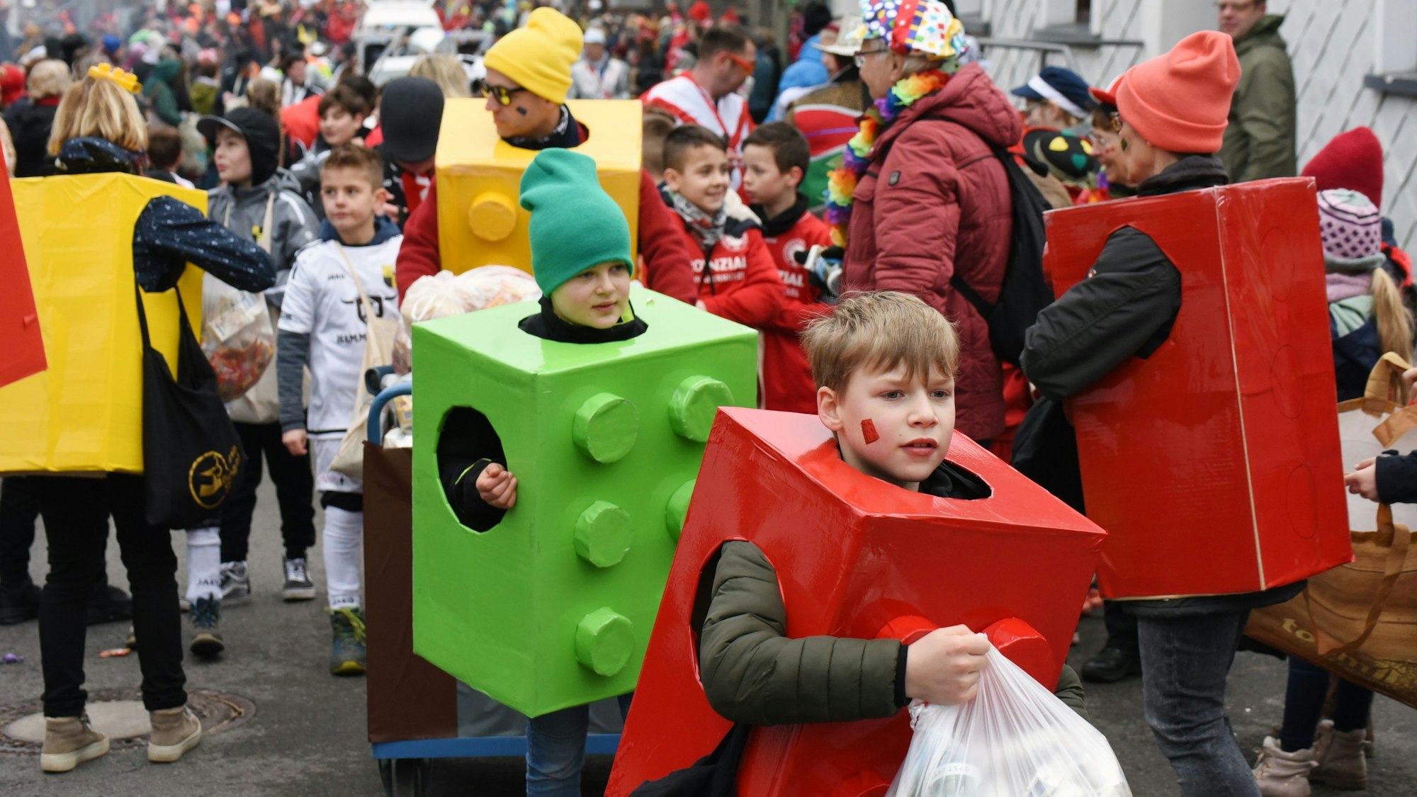 Mehrere Kinder sind als Legosteine verkleidet und tragen Kammelle in den Händen.
