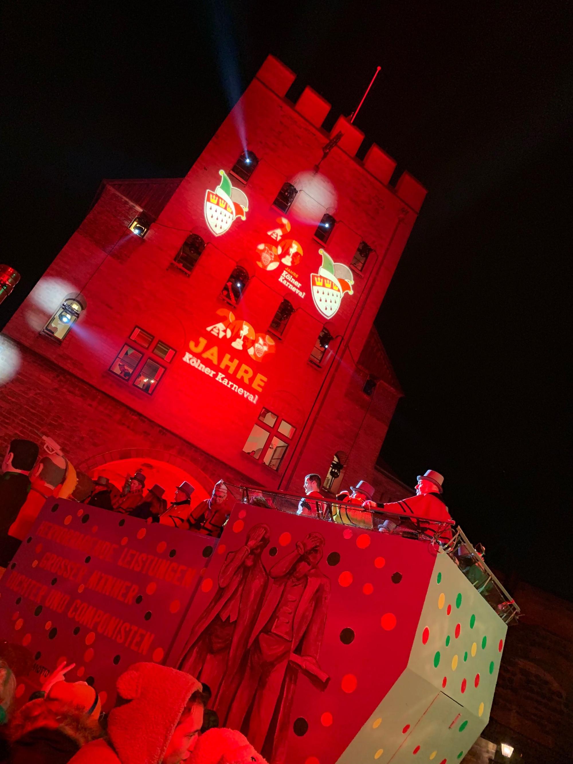 Die Severinstorburg strahlt rot: Die letzten Wagen passieren das Ziel des Rosenmontagszugs.