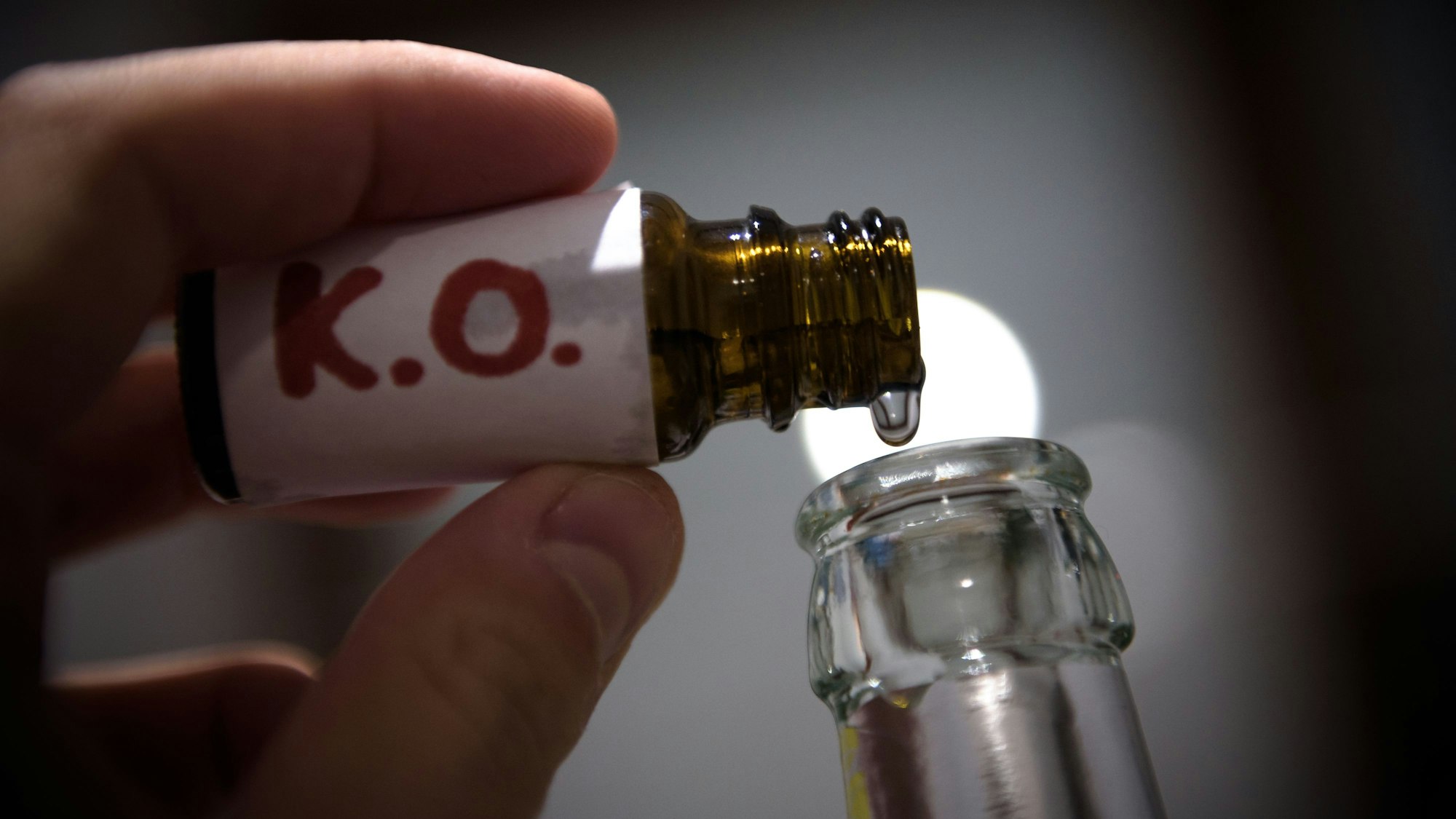 Ein Mann füllt in der gestellten Szene mehrere „K.O. Tropfen“ in eine Bierflasche.