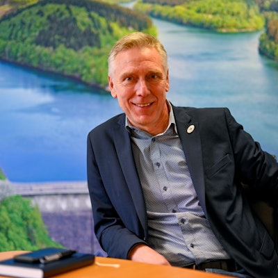 Dr. Uwe Moshage sitzt vor einer großen Luftaufnahme der Aggertalsperre.