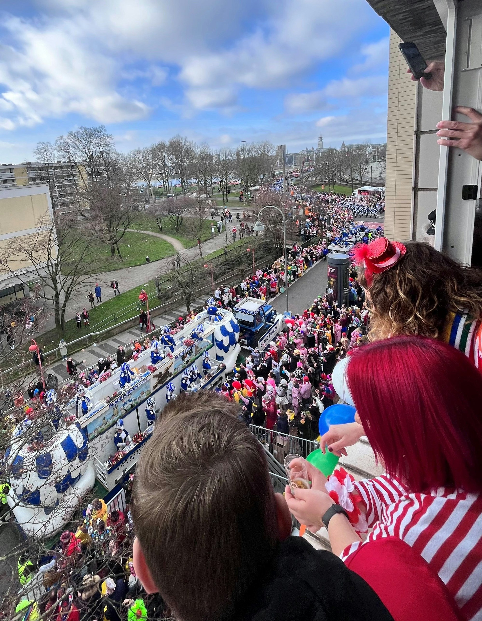 Der Blick über die Schulter der drei Feiernden hinunter auf den Zug, der auf der Deutzer Freiheit und über die Brücke geht.